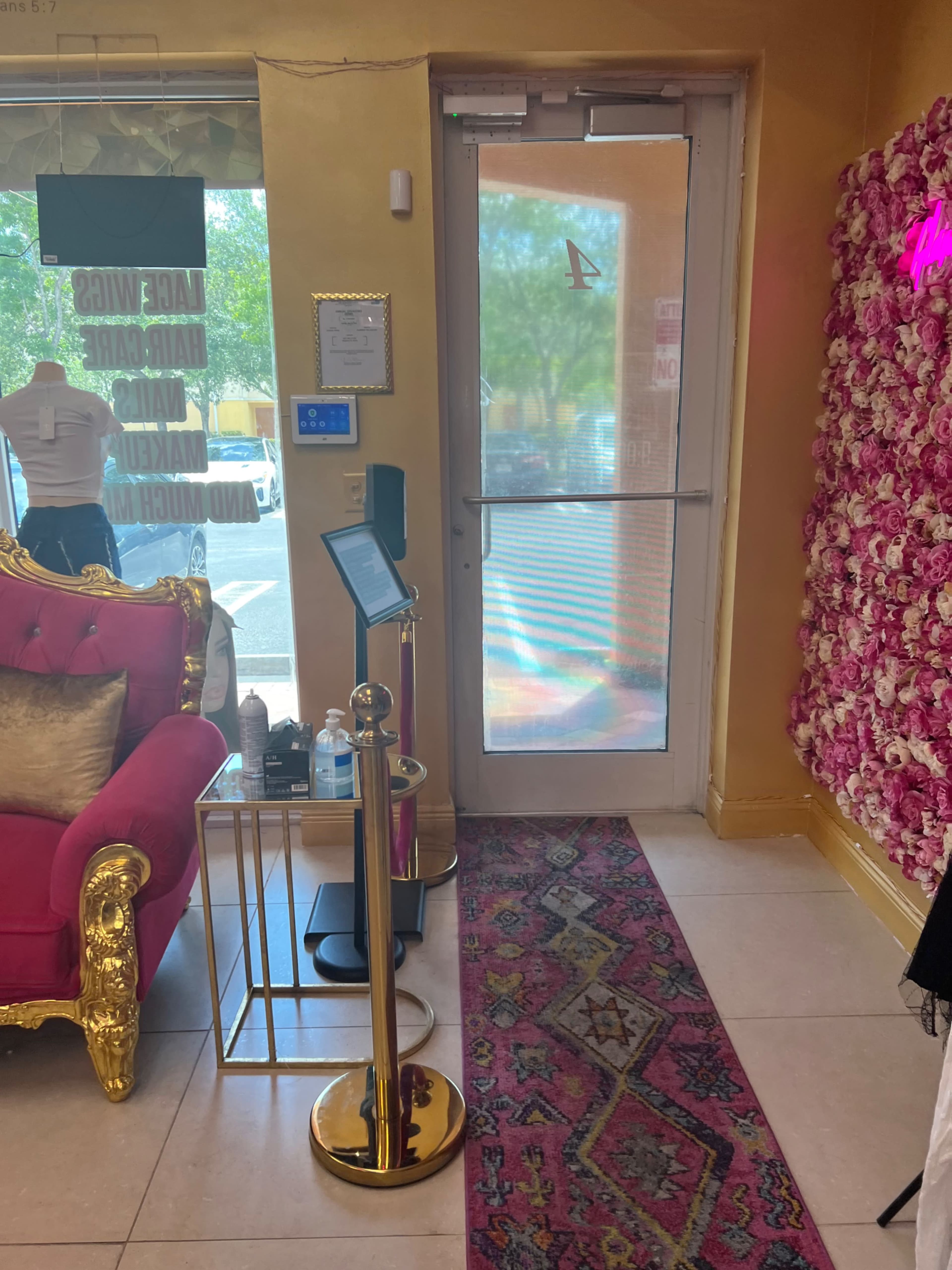 The image shows the interior of a brightly colored room featuring a pink velvet chair, a gold decorative stand, and a door with a transparent panel leading outside.