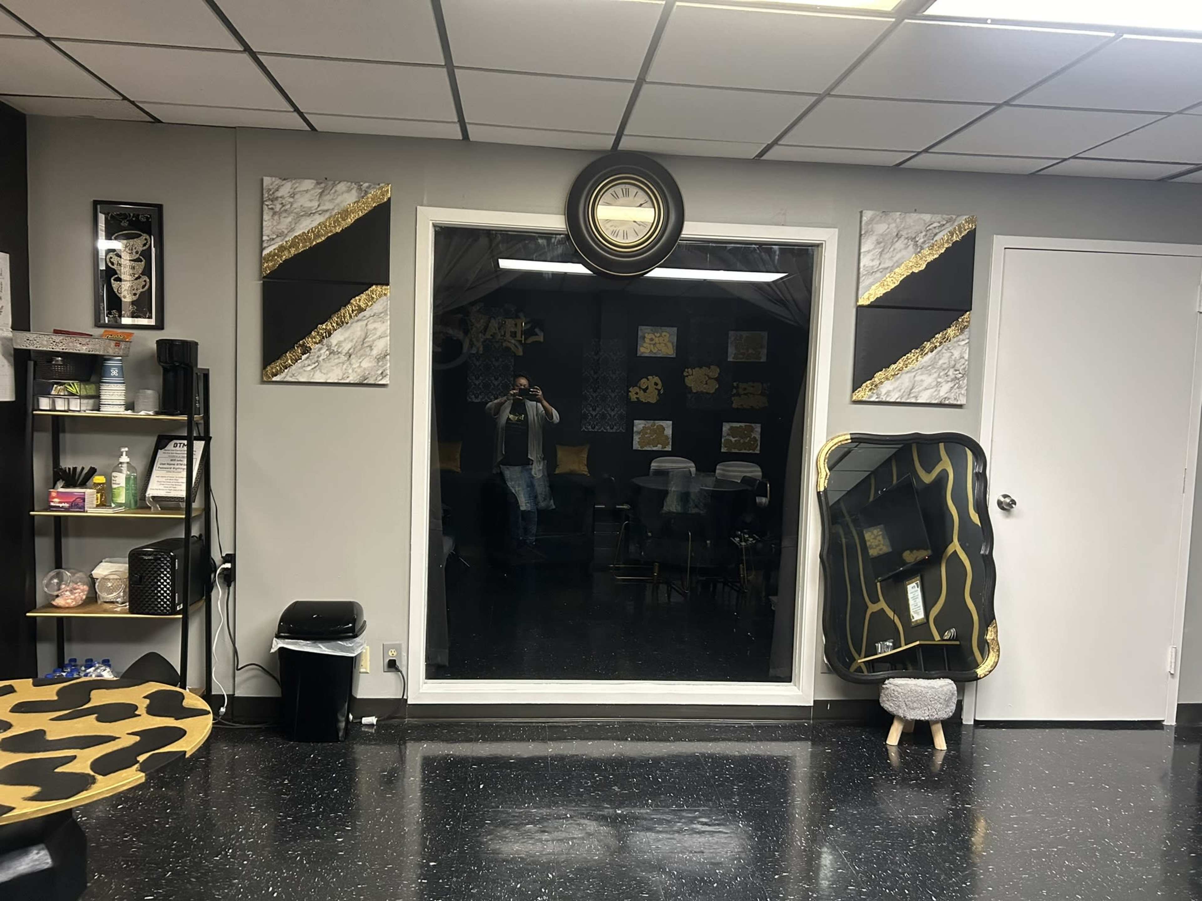 A room with black walls, a large mirror reflecting a person, and decorative artwork in gold and marble patterns.
