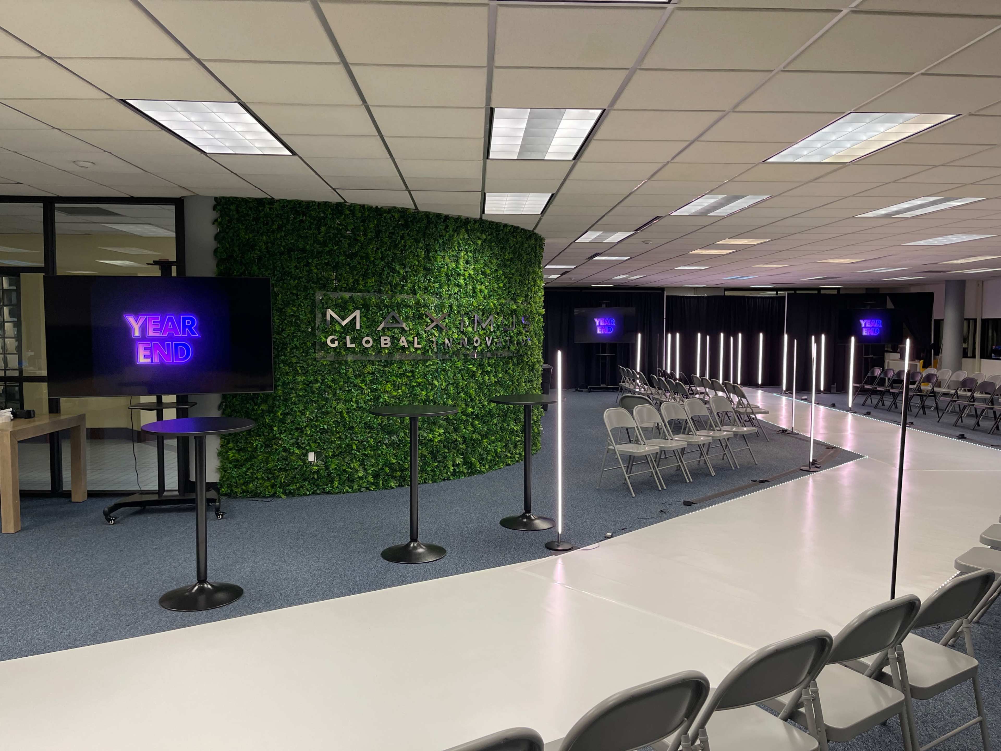 A modern event space with a greenery-covered wall, seating arranged in rows, and screens displaying "YEAR END."