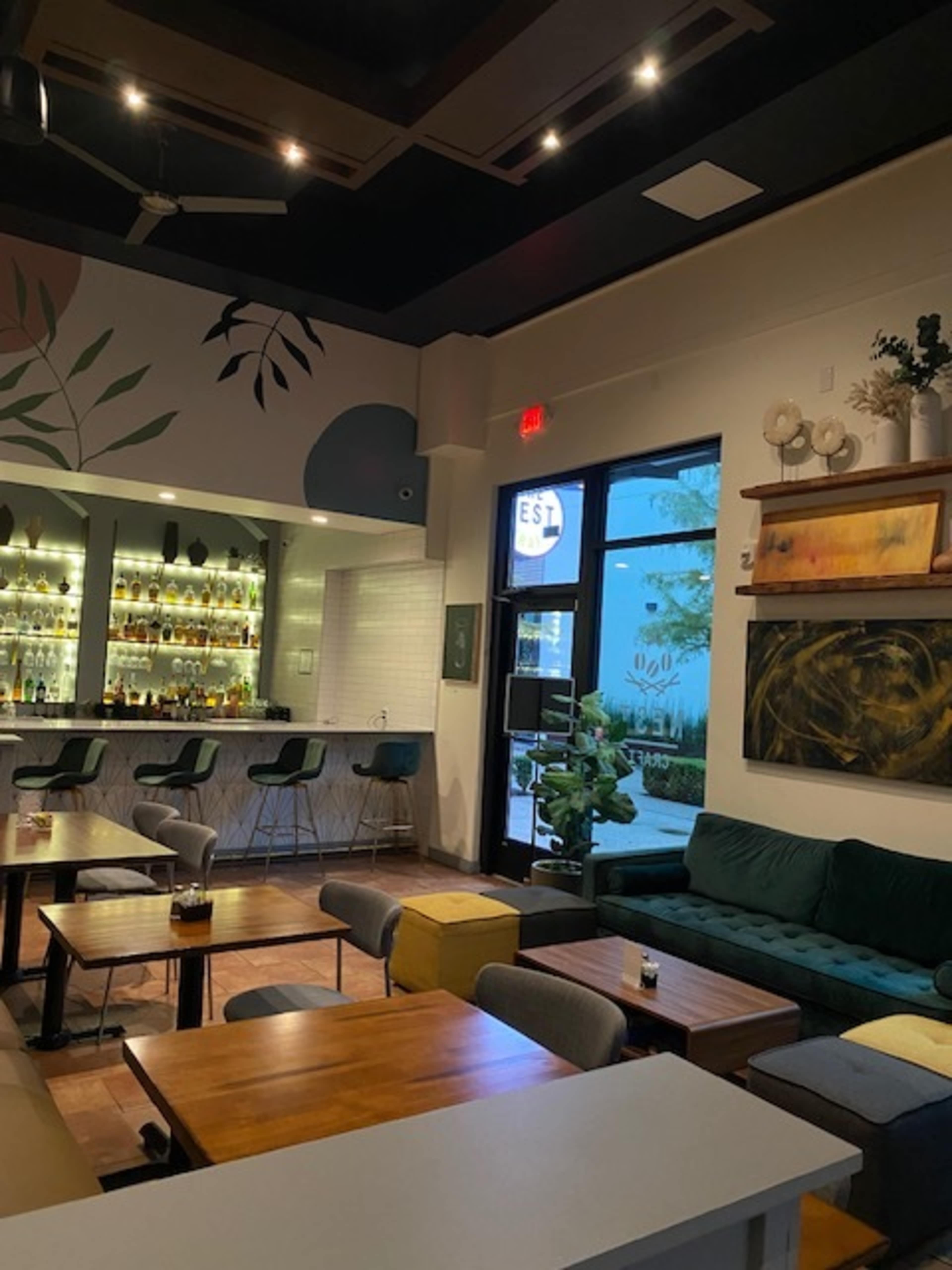 The image shows a modern bar interior with a variety of seating options and a well-stocked backlit bar.