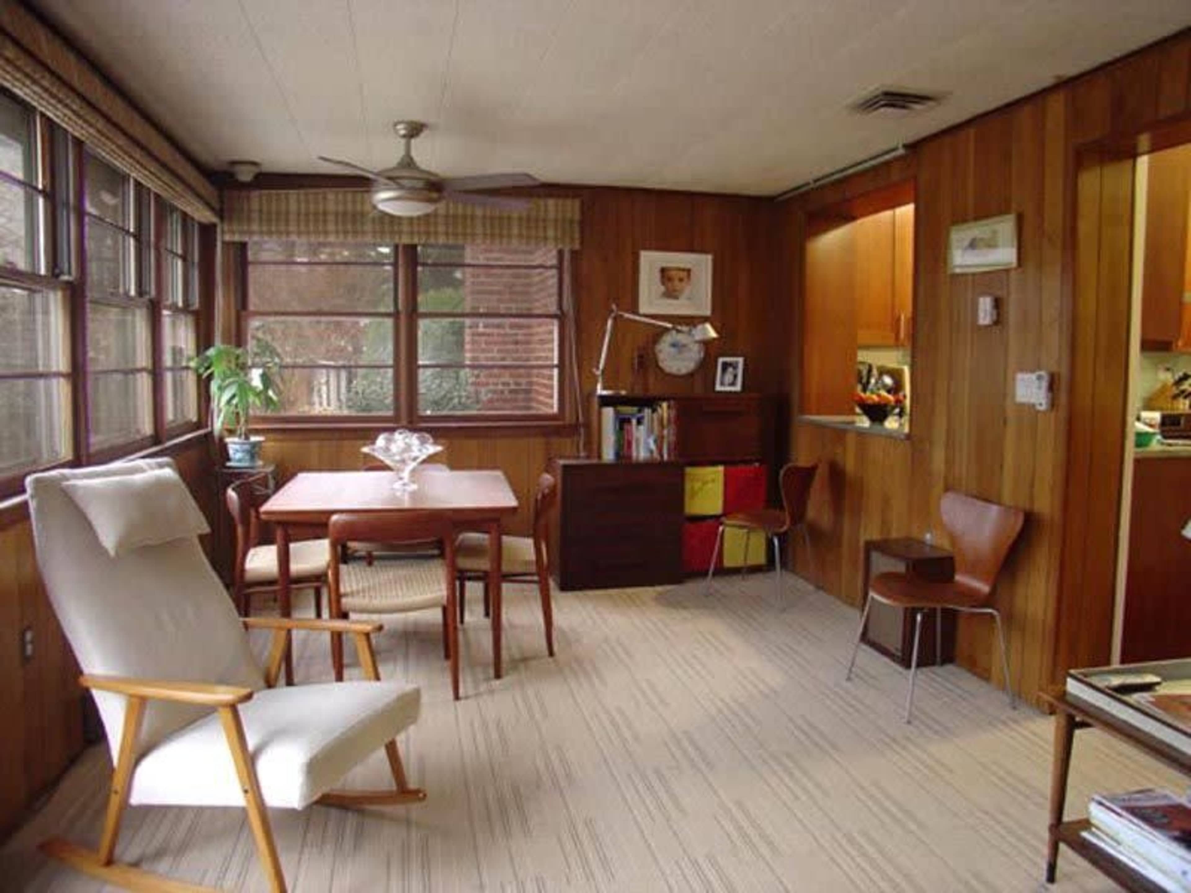 A wooden-paneled room with a dining table, chairs, and a small kitchen area visible in the background.