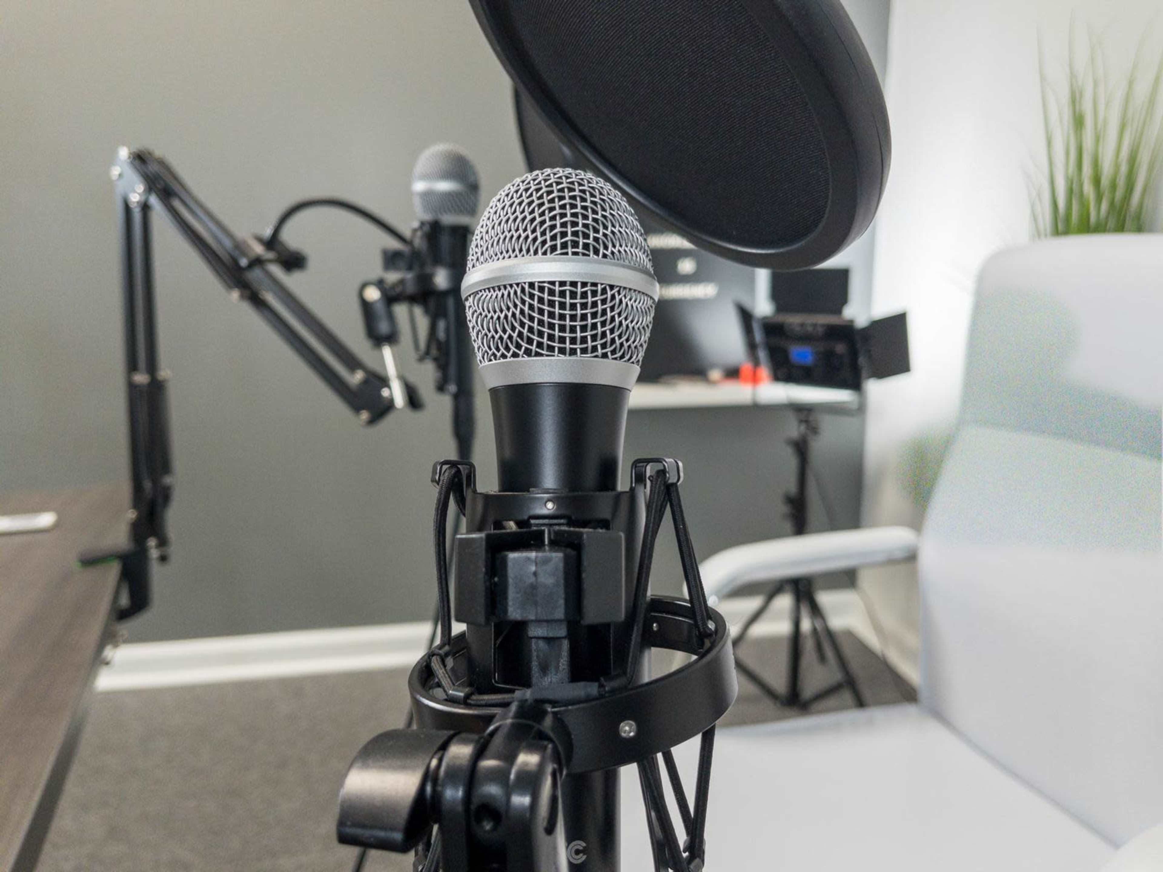 A close-up of a microphone mounted on a stand, with another microphone and a chair visible in the background.