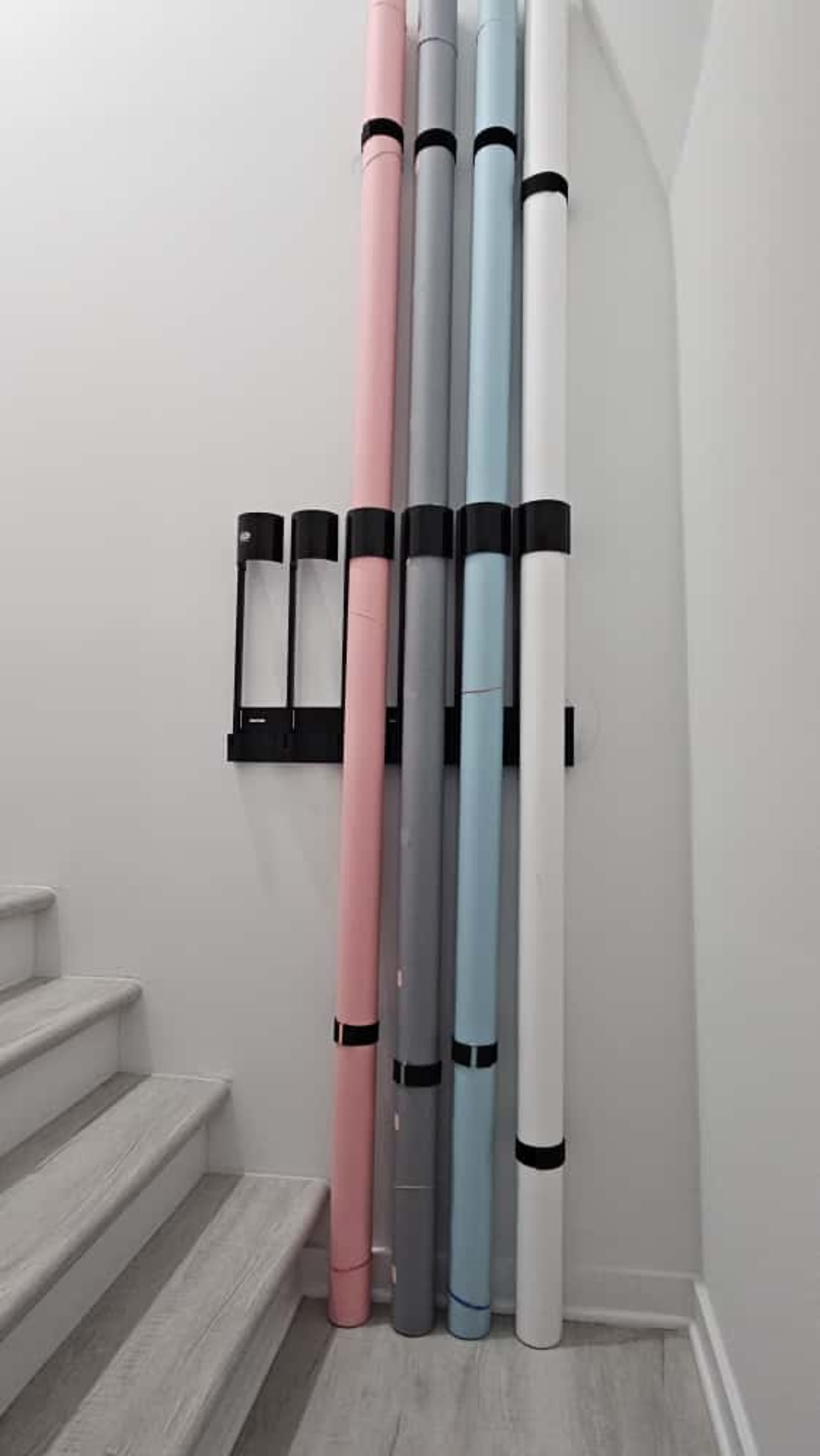 A series of rolled paper tubes in various colors stands upright against a wall next to a staircase.
