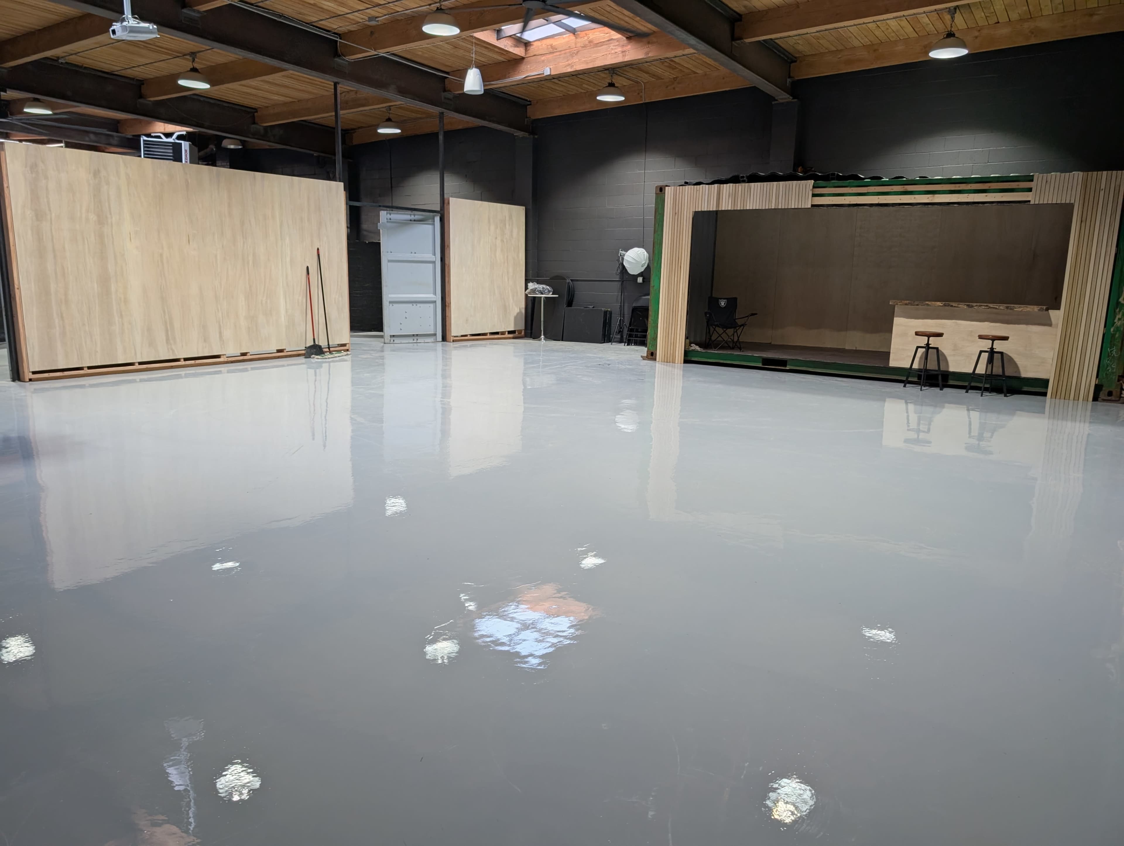 The image shows a spacious, empty warehouse with a shiny gray concrete floor and wooden structures along the walls.
