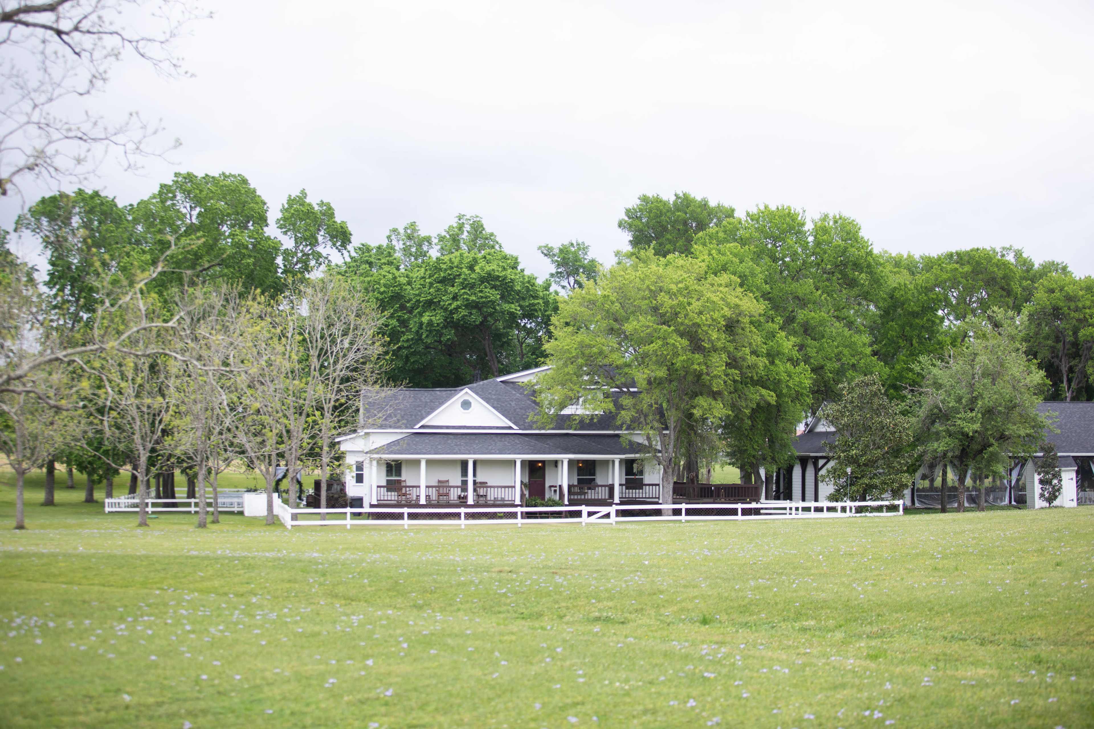 A large white house with a porch is surrounded by green trees and a grassy lawn.