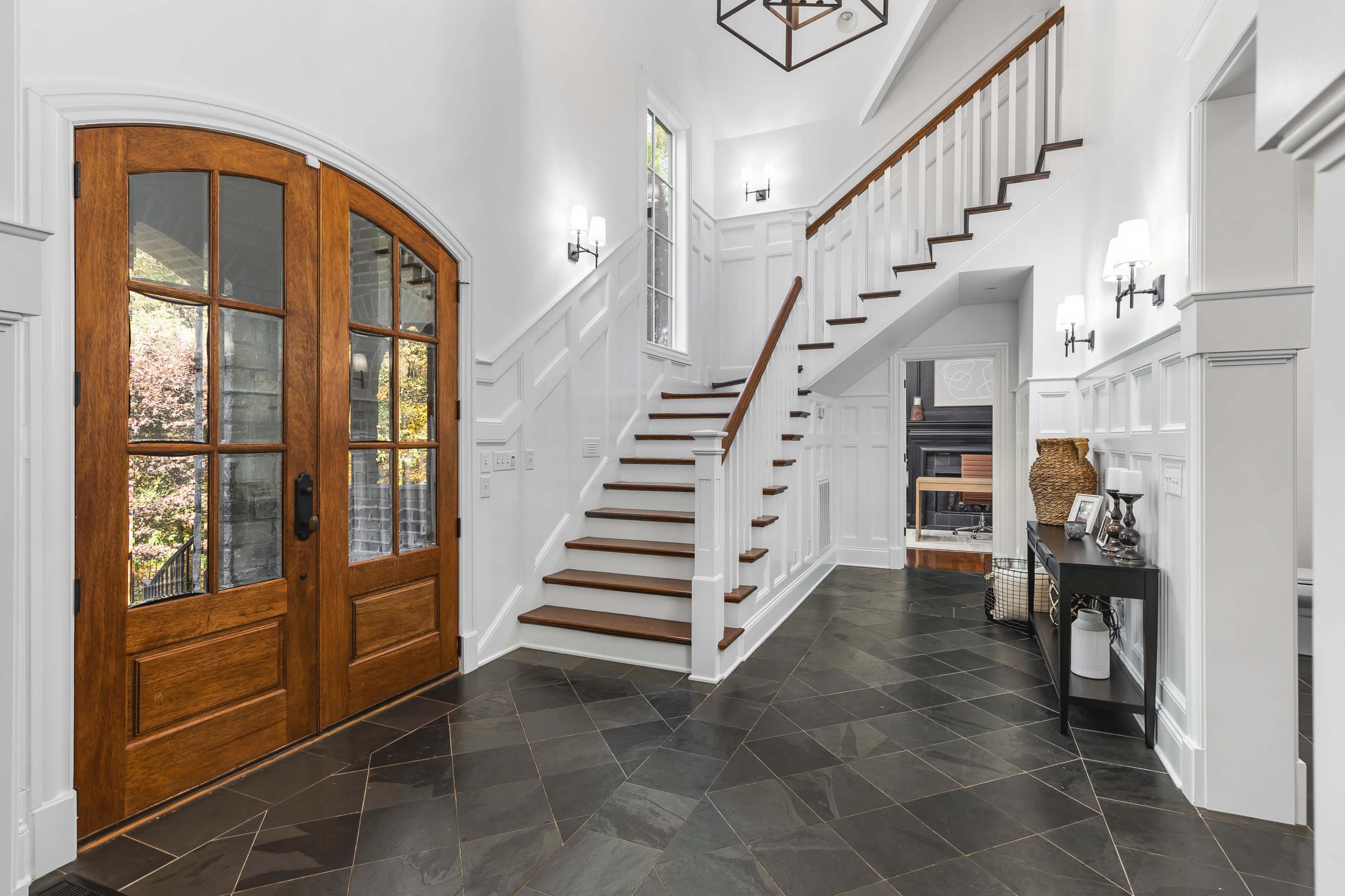 A bright foyer with a wooden front door, a staircase, and black slate flooring.