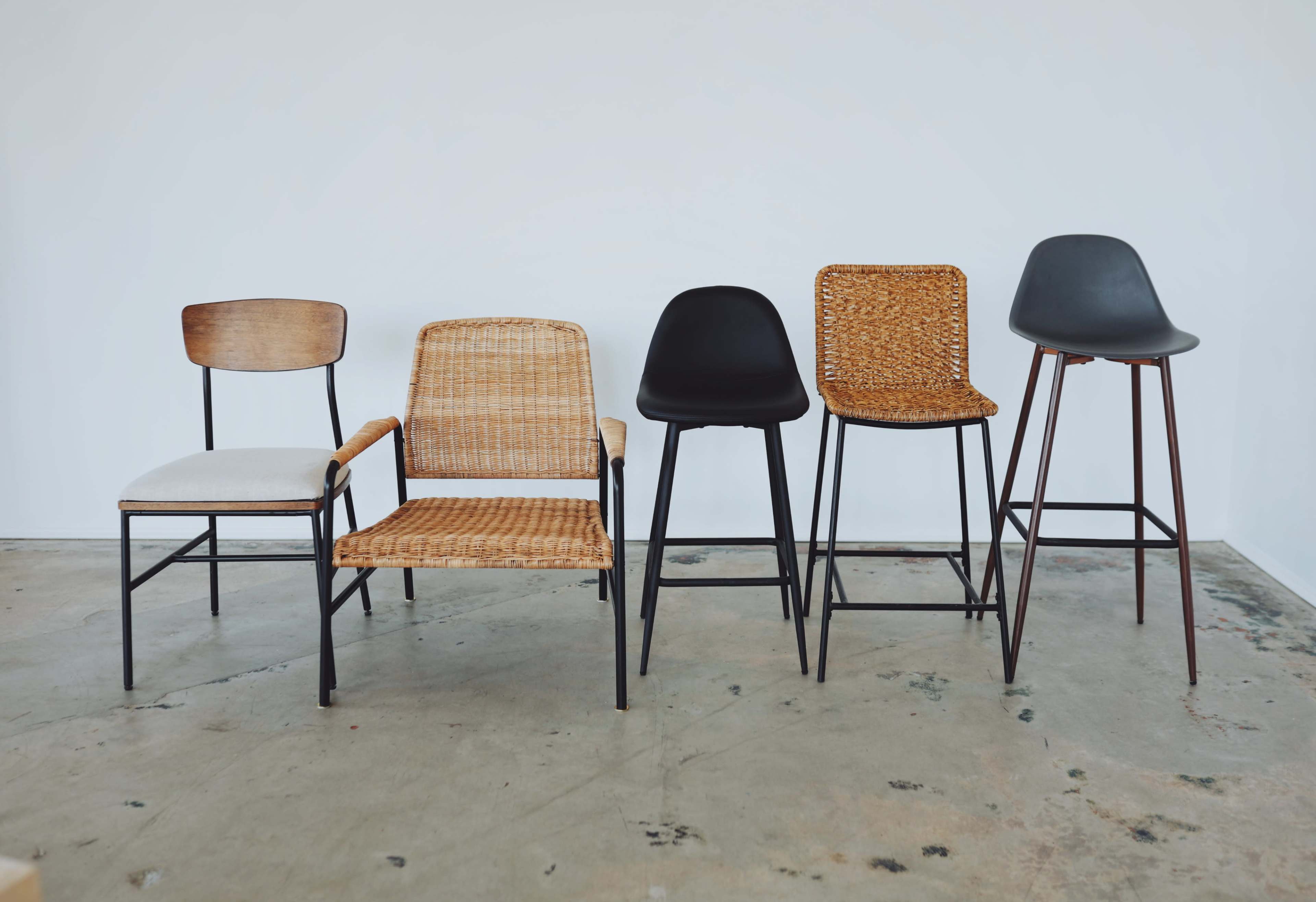 Five chairs of varying styles and heights arranged in a row against a plain white wall.