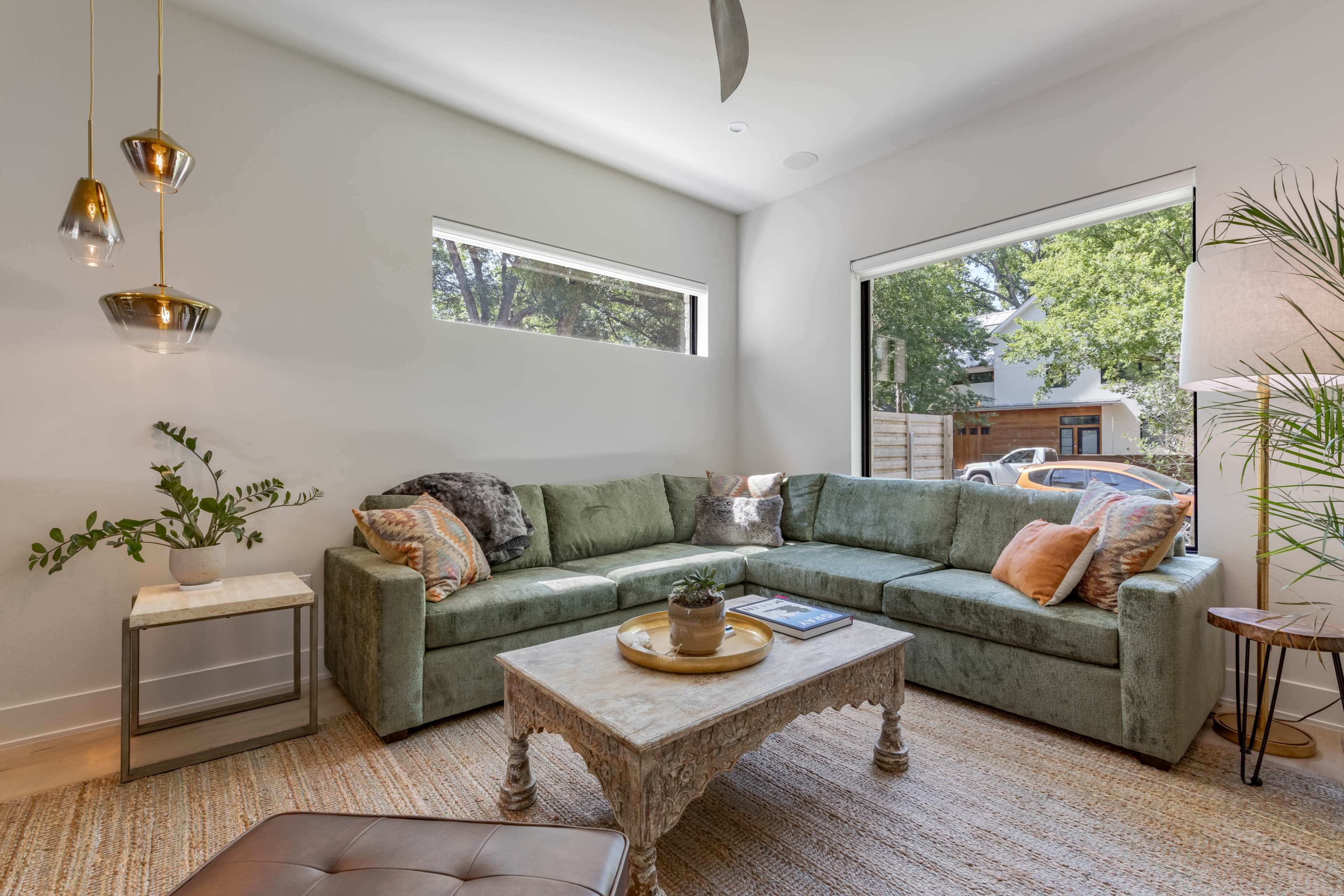 A green sectional sofa is positioned in a brightly lit living room with large windows and a decorative coffee table.