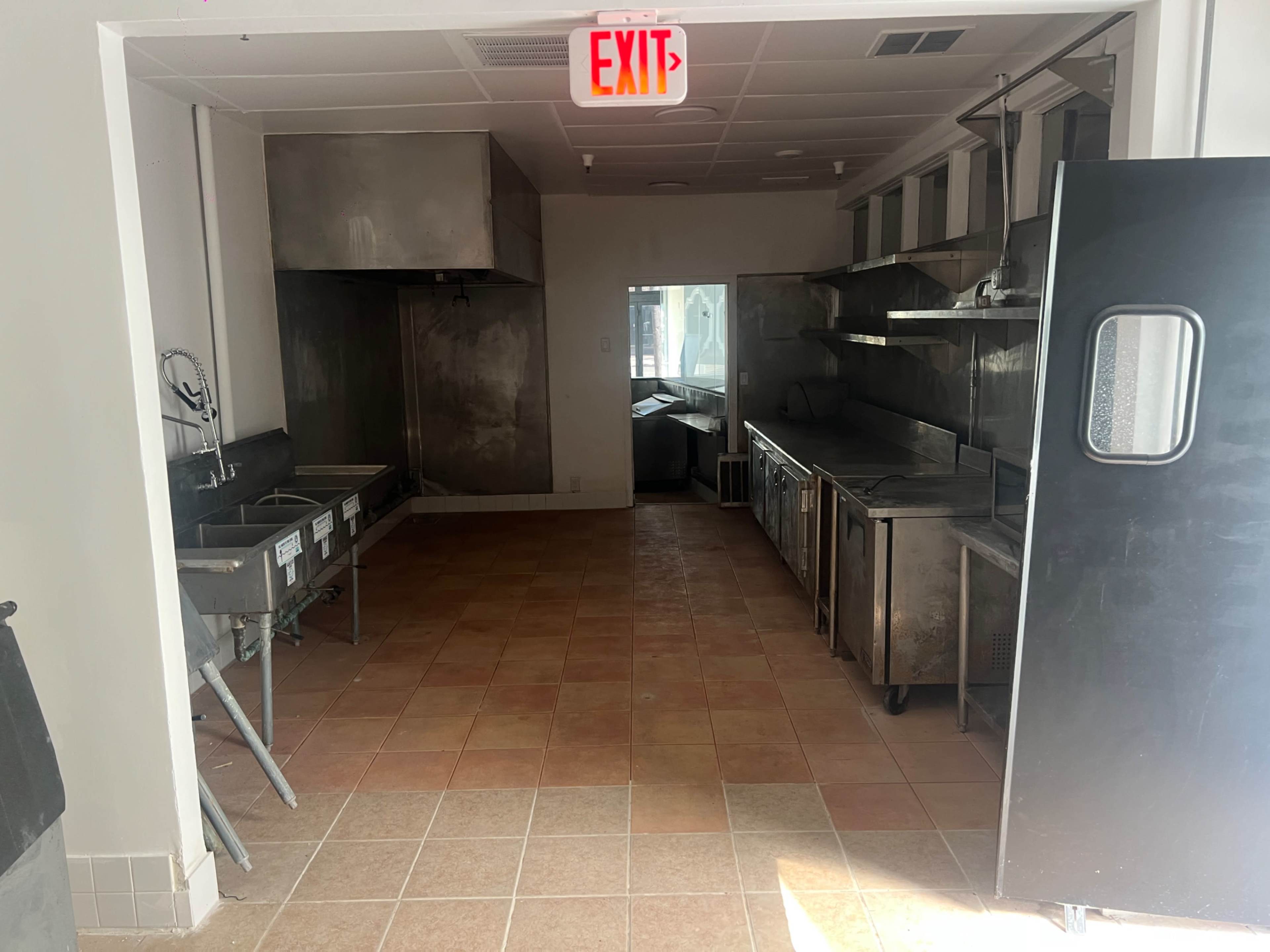 The image shows an empty commercial kitchen space with stainless steel appliances and tiled flooring.