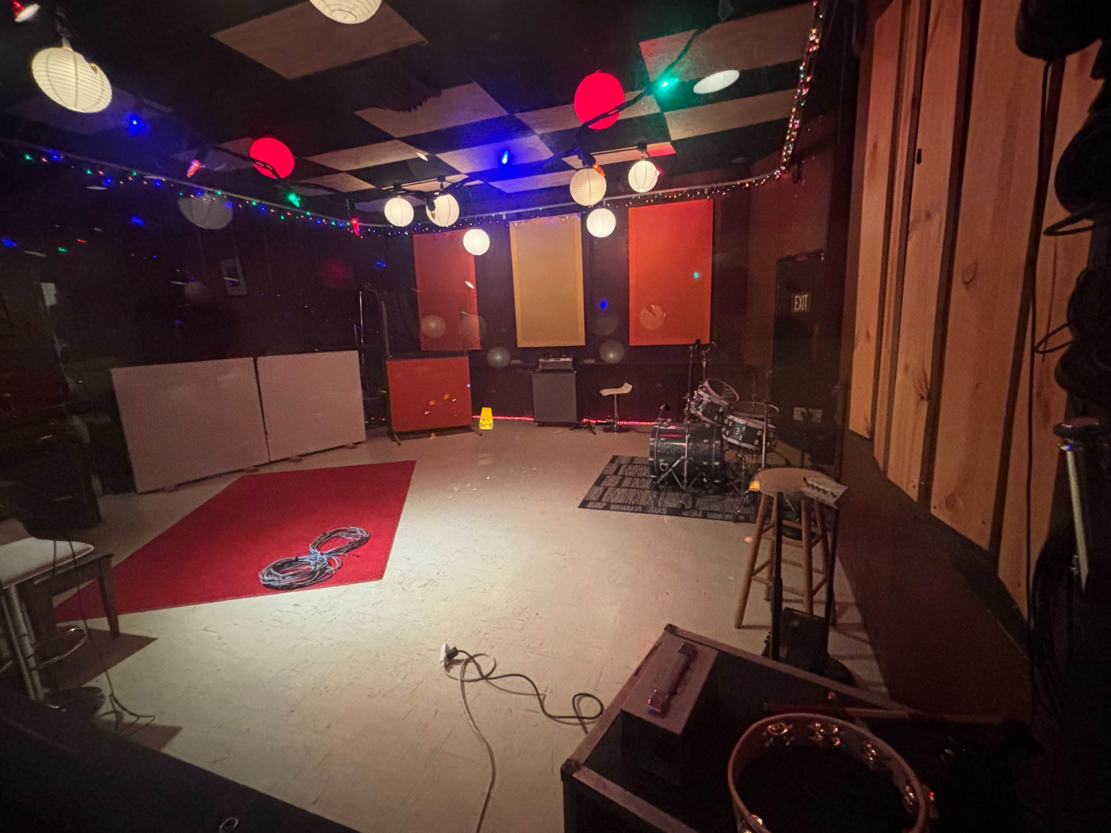 The image shows a music rehearsal space with a red carpet, drum set, and colorful decorative lights.