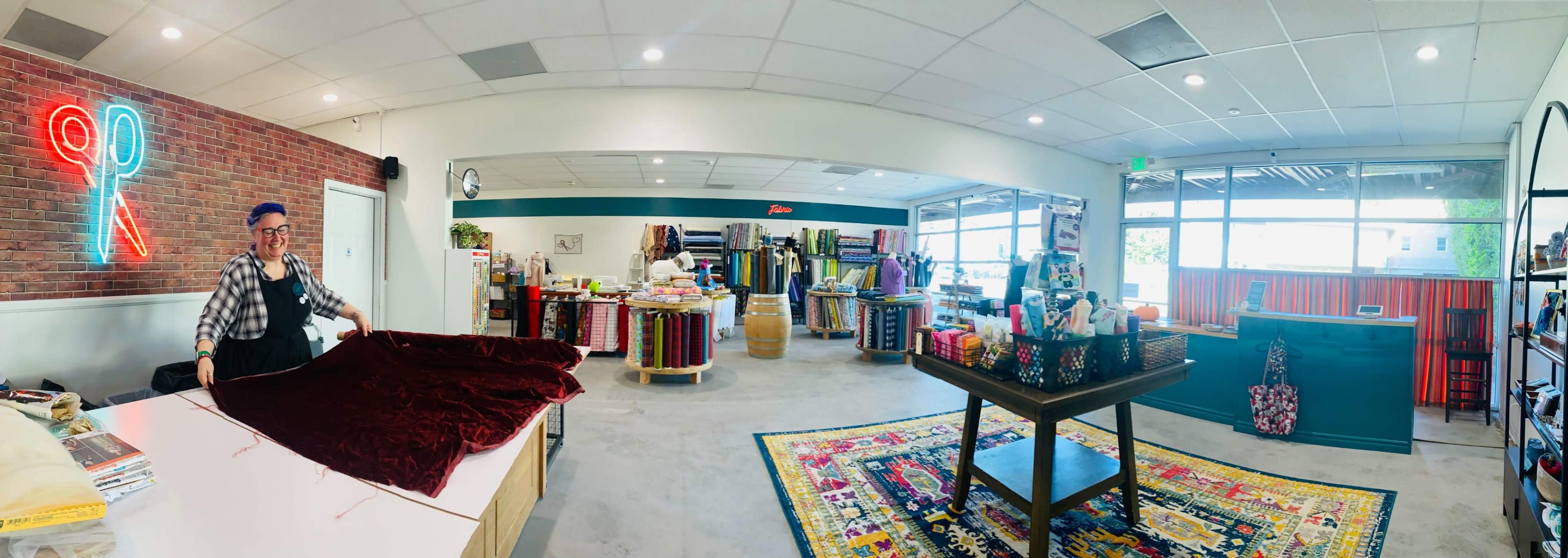 A fabric store features a colorful array of materials, with a worker folding a piece of red fabric at a central table amid vibrant displays and shelves.