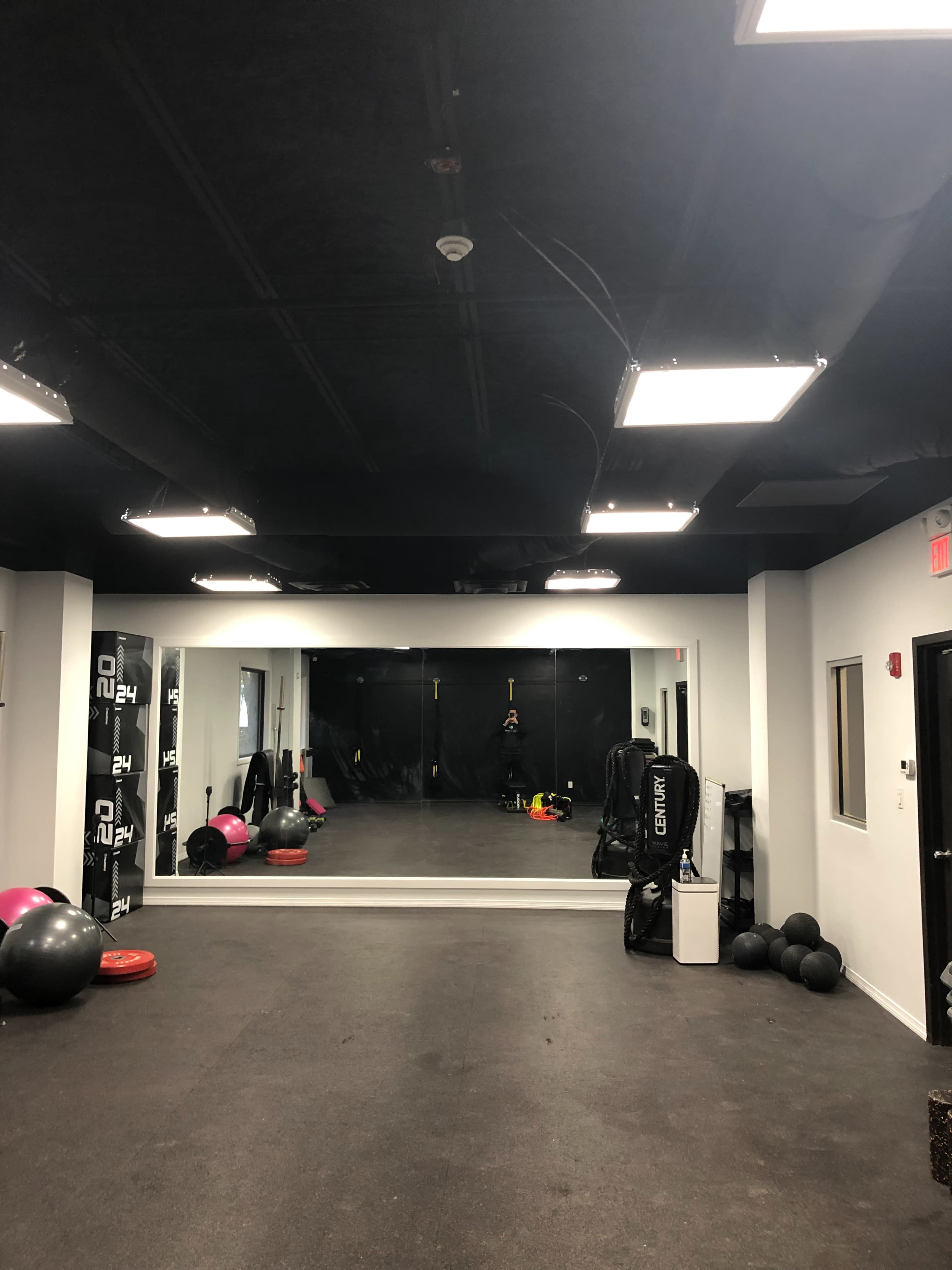 The image shows a fitness training room with a large mirror, various exercise equipment, and a black ceiling.