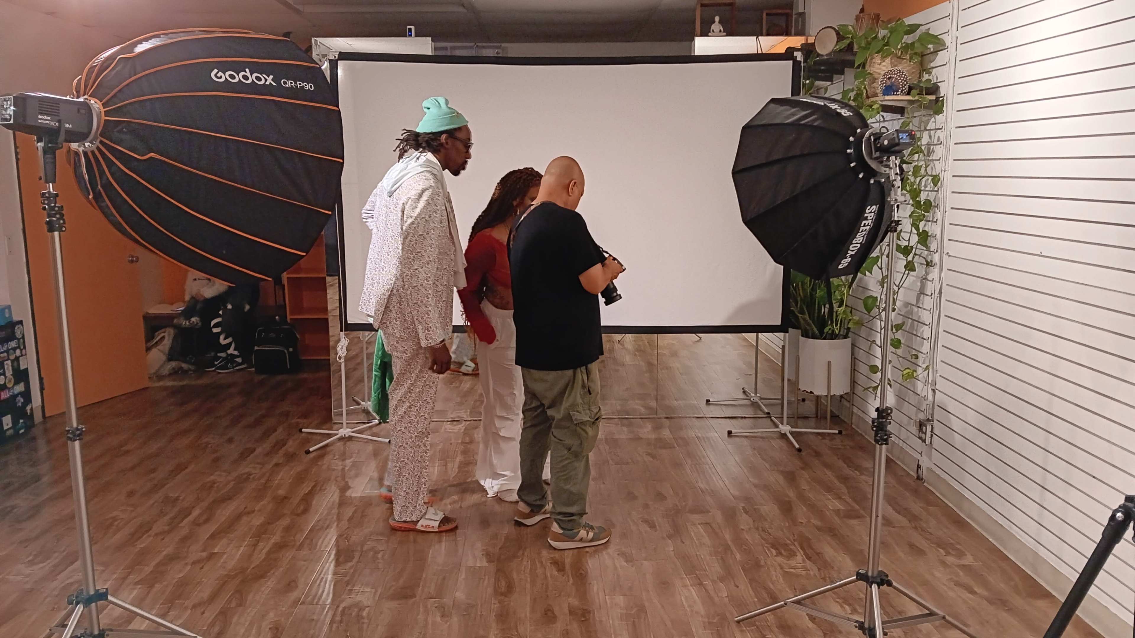 A group of three people stands in front of a backdrop in a photography studio, surrounded by lighting equipment.