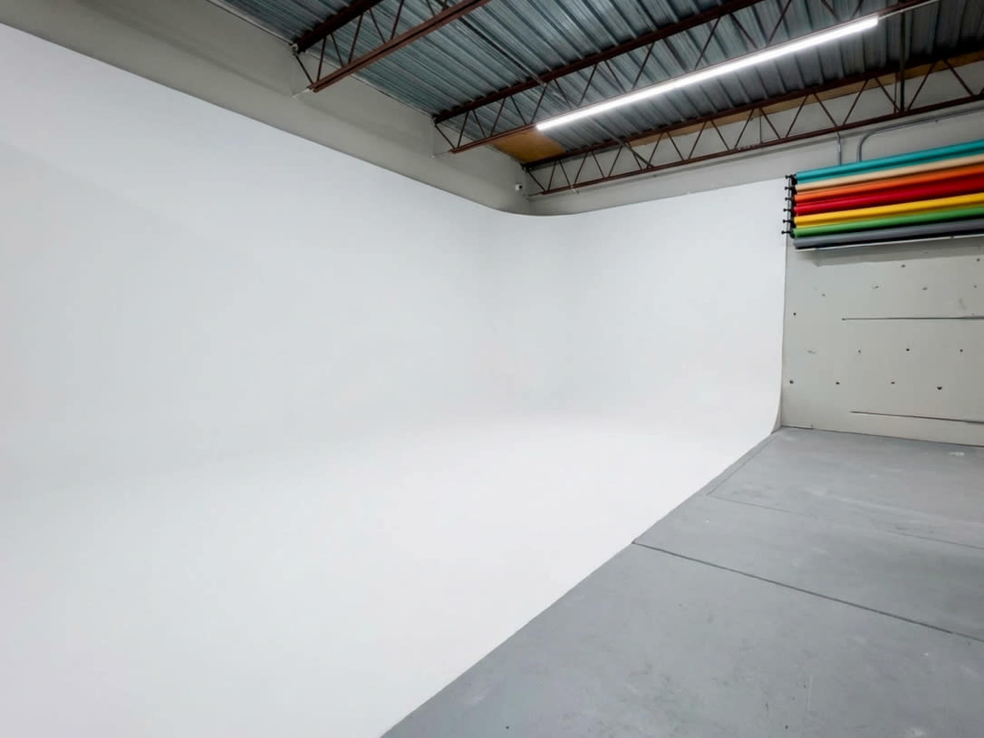 The image shows a spacious studio with a seamless white backdrop and a wall featuring colorful rolled backdrops.