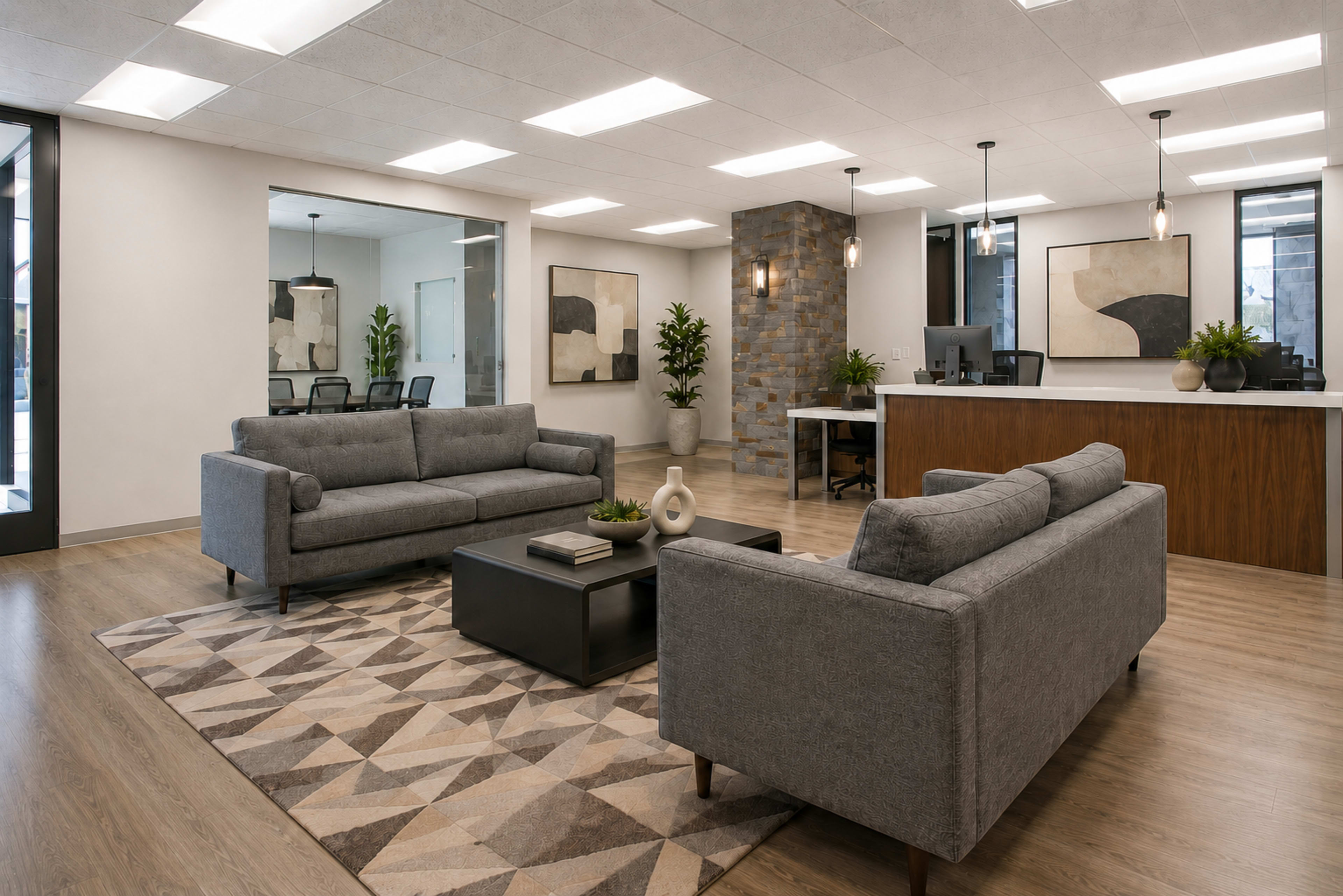 The image shows a modern office reception area with two gray sofas, a coffee table, a decorative rug, and a reception desk behind it.