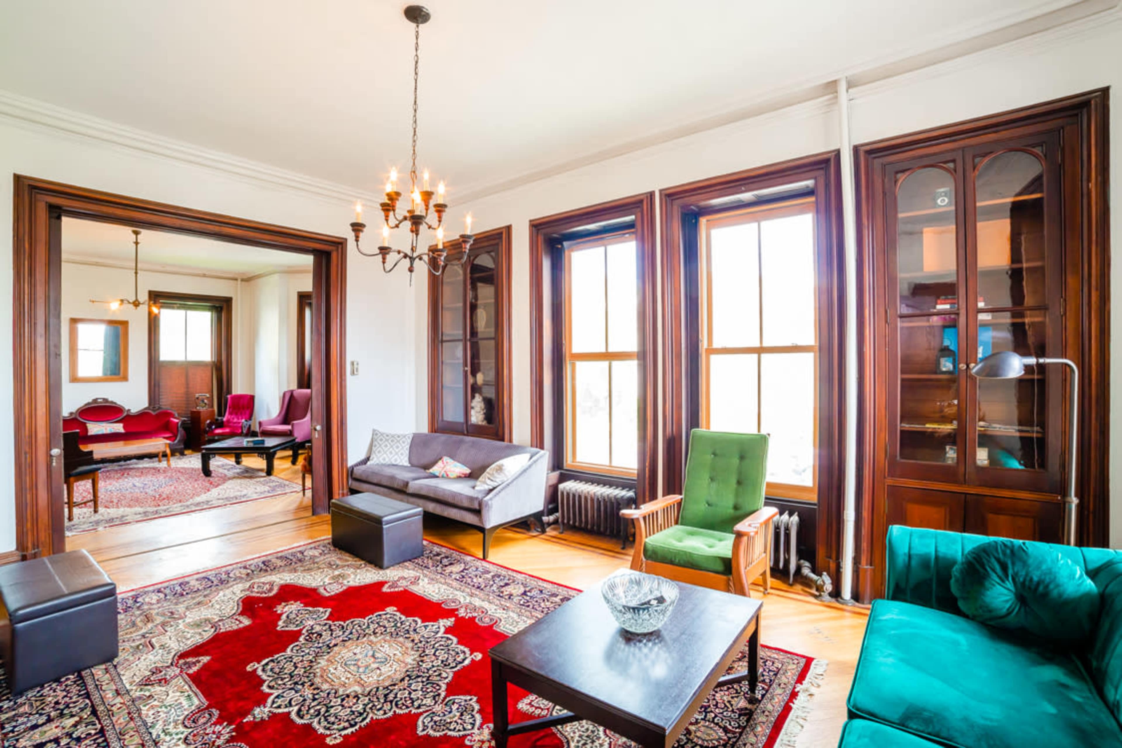 A spacious living room with a decorative red and cream area rug, multiple seating options, and large windows allowing natural light to fill the space.