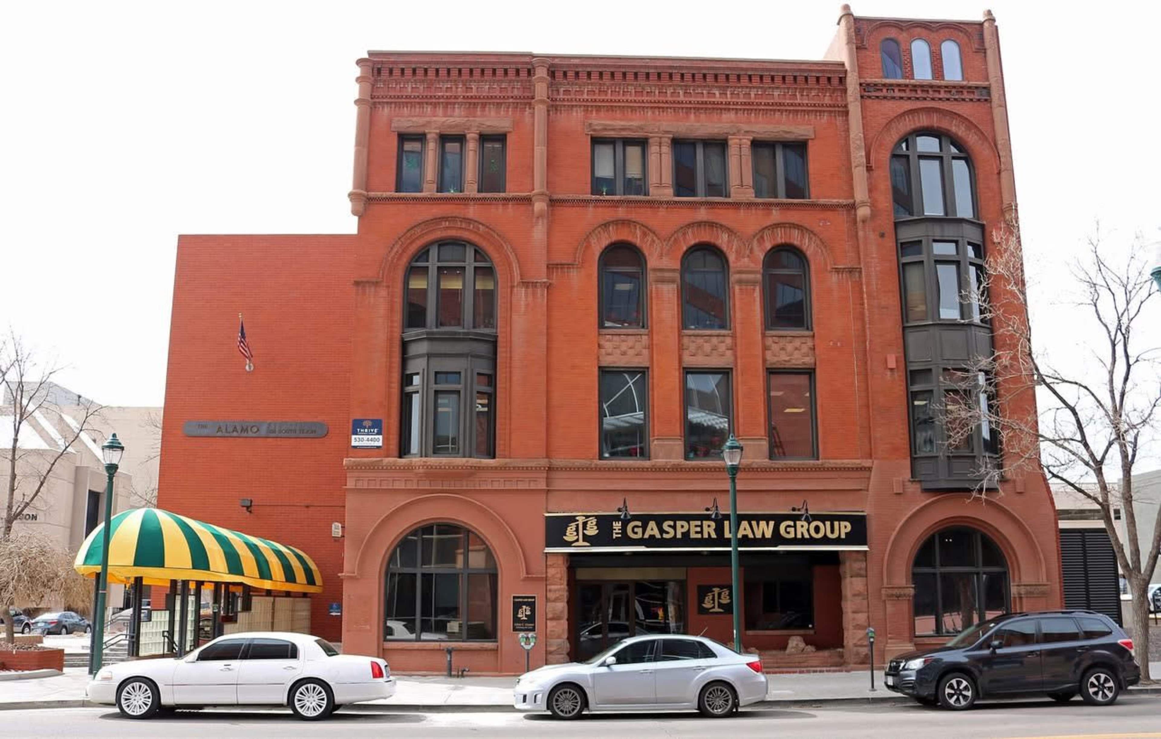 The image depicts a historic red brick building housing the Gasper Law Group, with a distinctive green and yellow striped awning at the entrance.