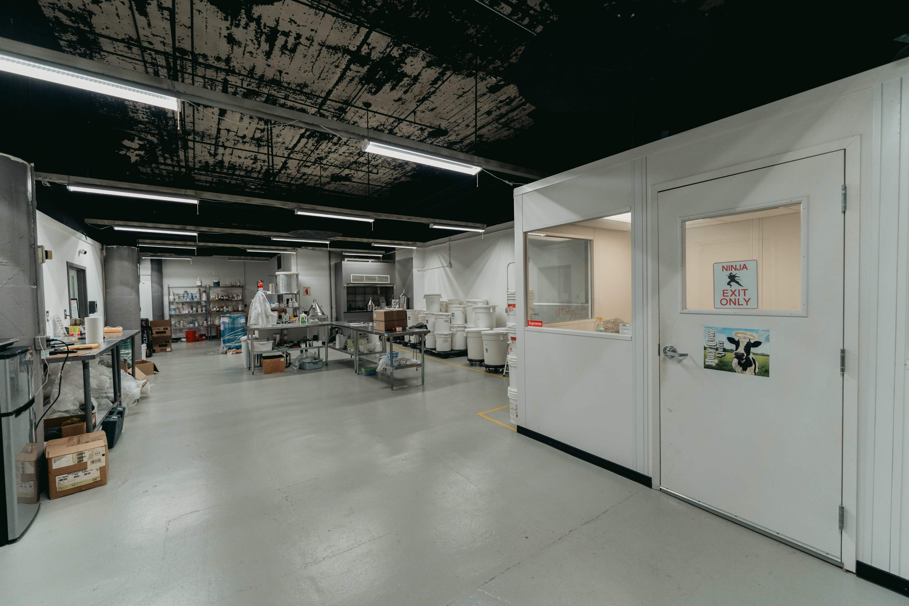 A spacious commercial kitchen with stainless steel appliances, workstations, and storage areas, featuring an exit door labeled "EXIT ONLY."