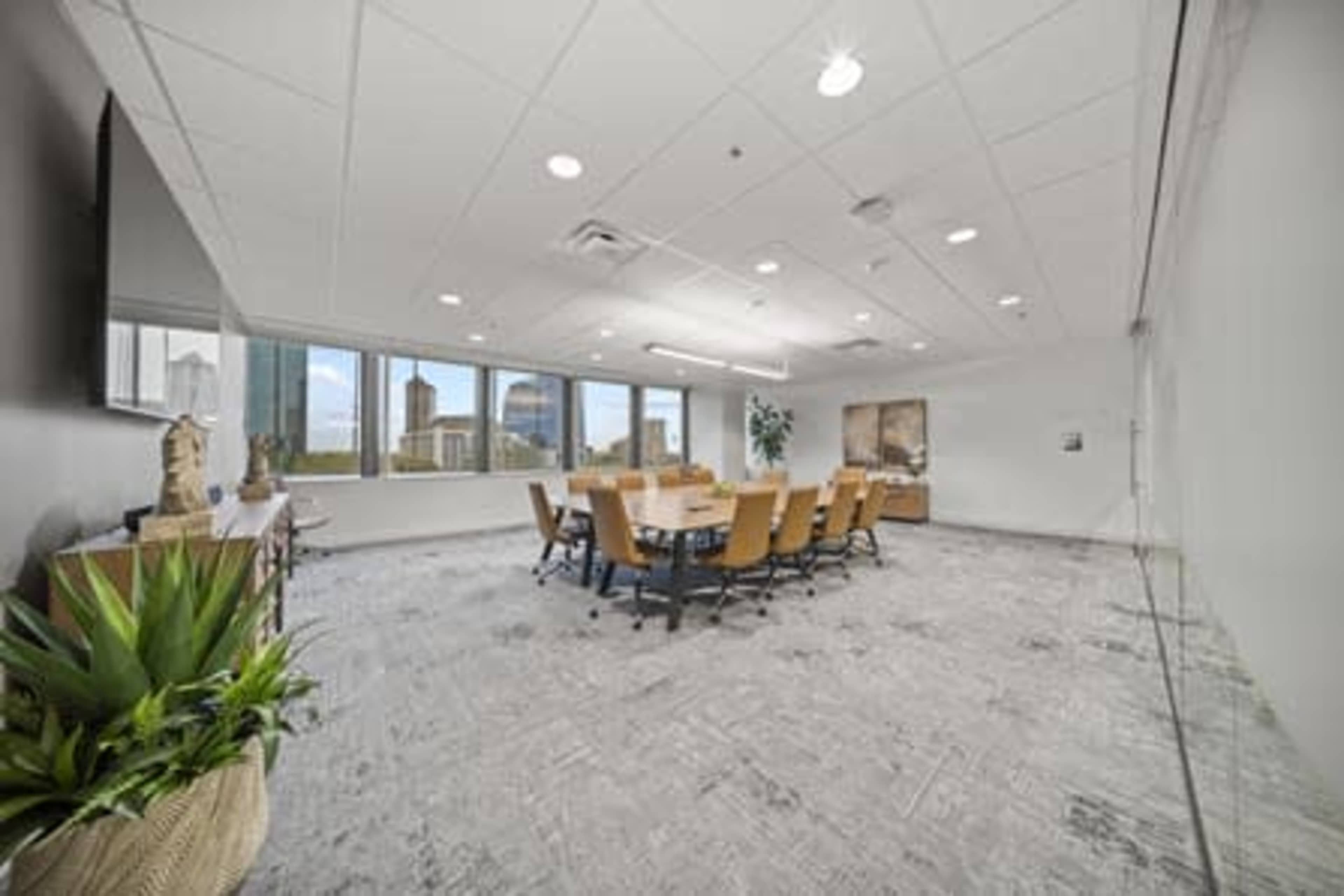 The image shows a modern conference room with a large oval table surrounded by chairs and windows offering a view of a city skyline.