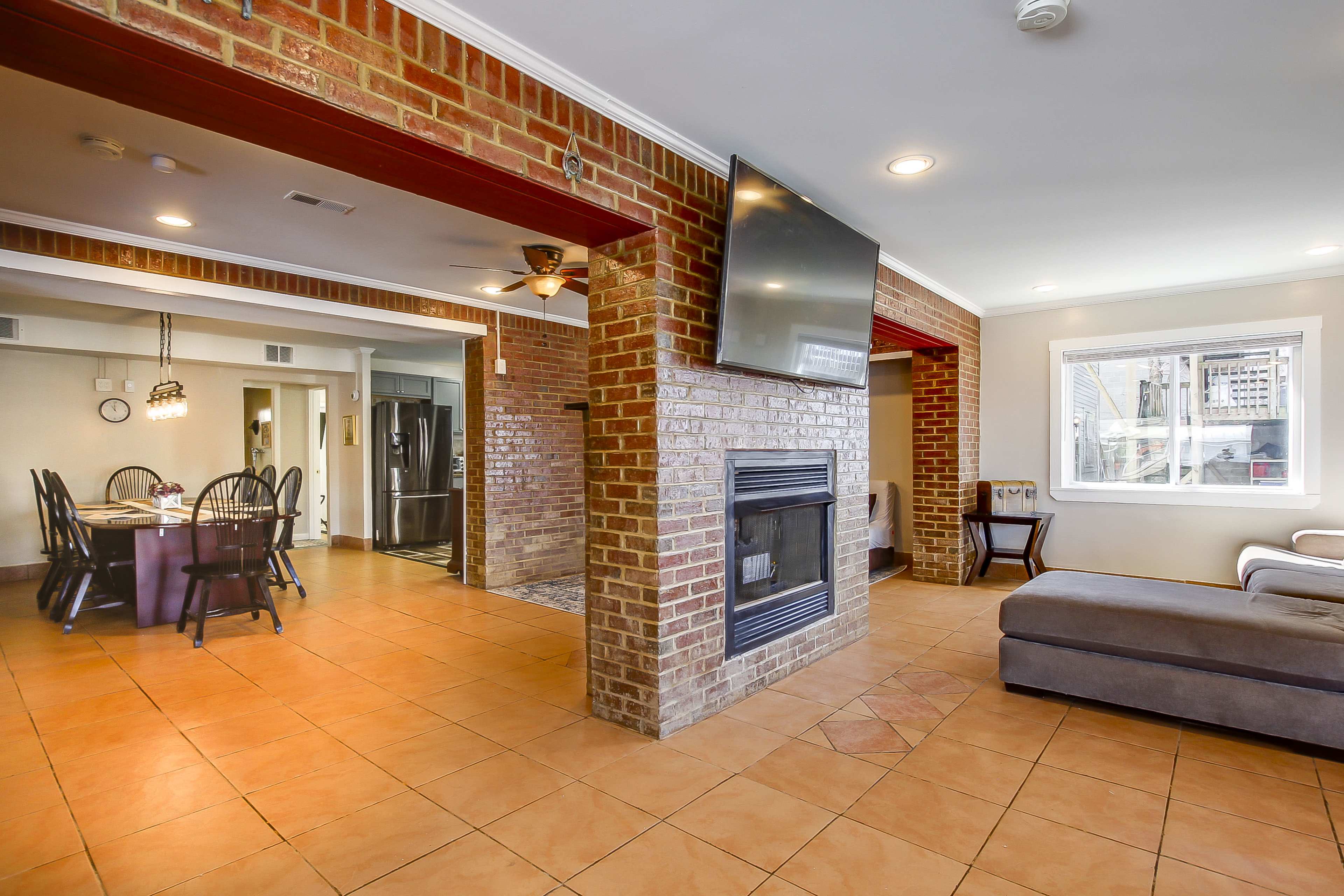 A spacious living area with a brick fireplace, a flat-screen TV mounted on the wall, and a dining area visible in the background.
