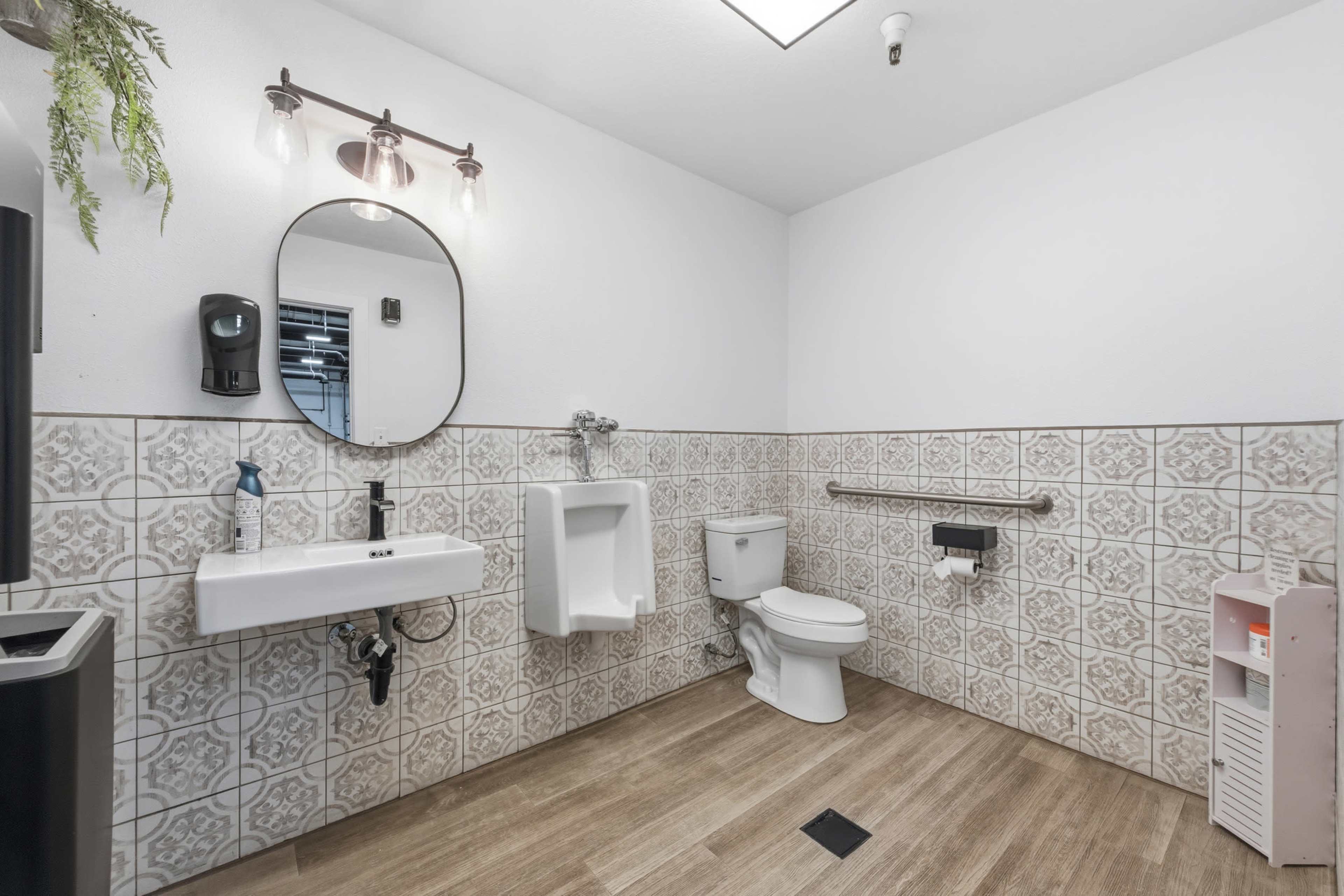 The image shows a clean bathroom featuring a wall-mounted sink, a urinal, a toilet, and tiled walls with a patterned design.