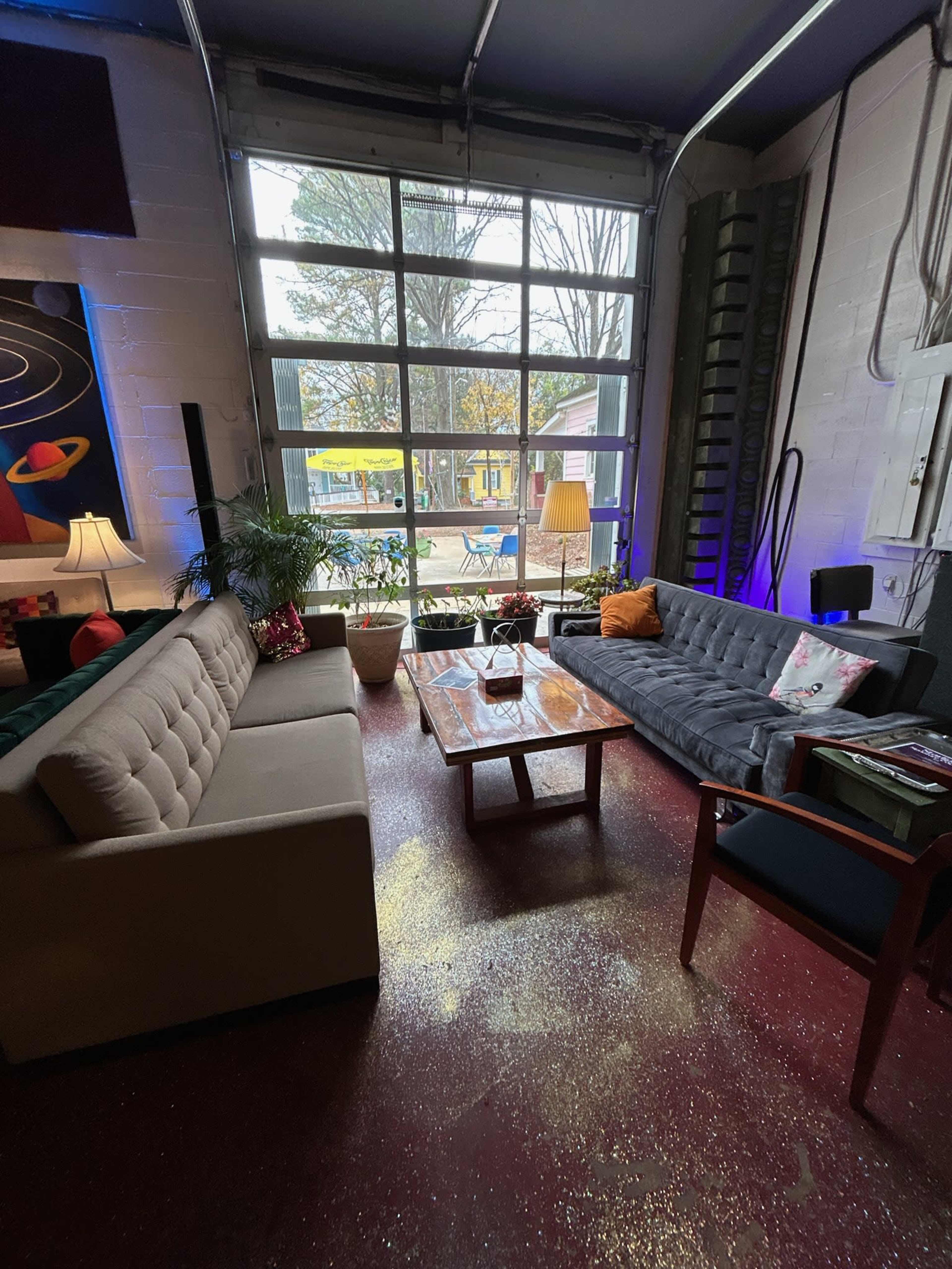 A cozy lounge area features two sofas, a coffee table, and large windows overlooking a garden outside.
