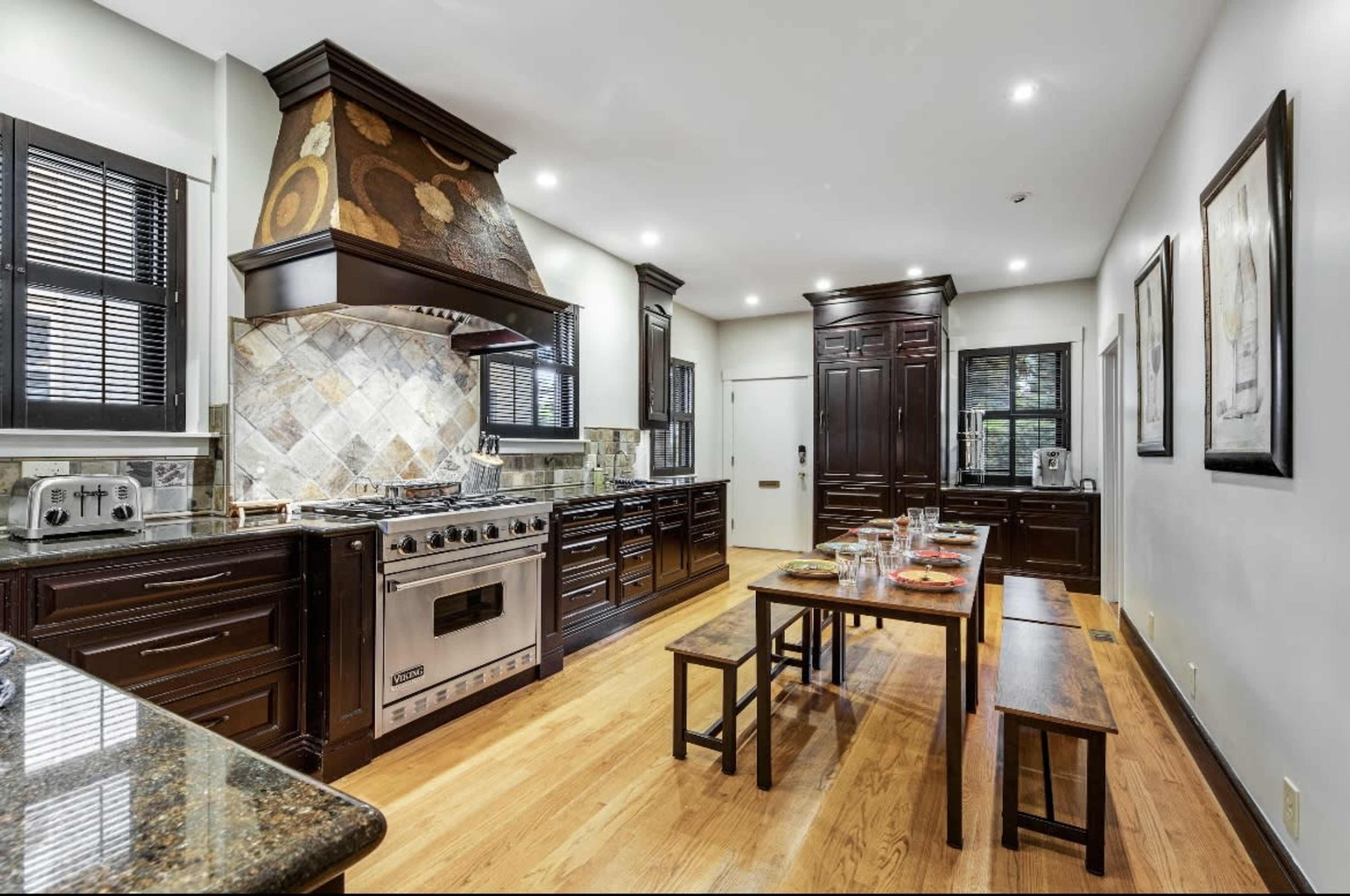 A modern kitchen featuring dark wooden cabinetry, a large stainless steel range, and a dining area with wood benches and a table set for a meal.
