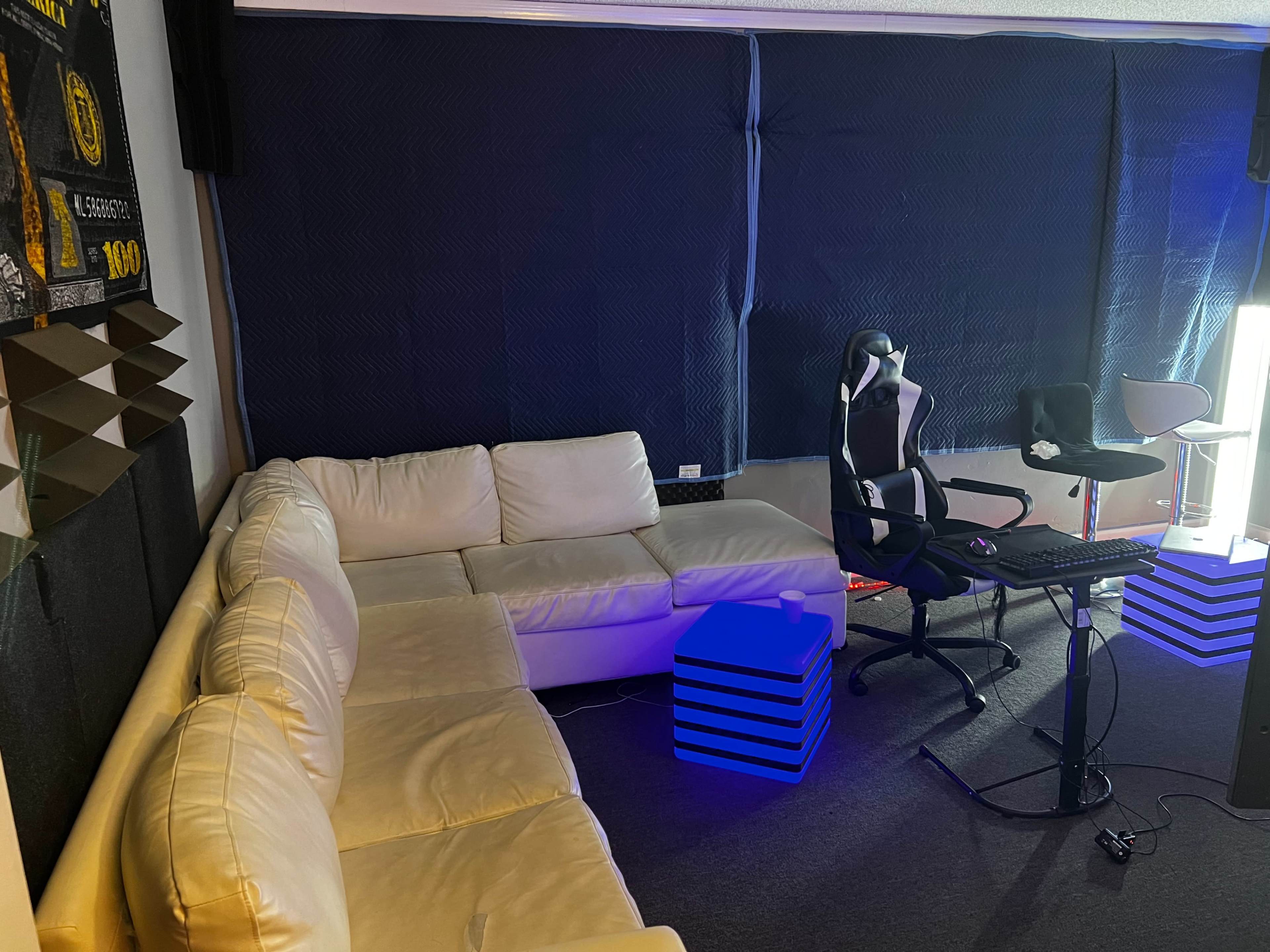 The image shows a room with a white sectional couch, a gaming chair, a desk with a keyboard, and blue-lit decorative cubes.