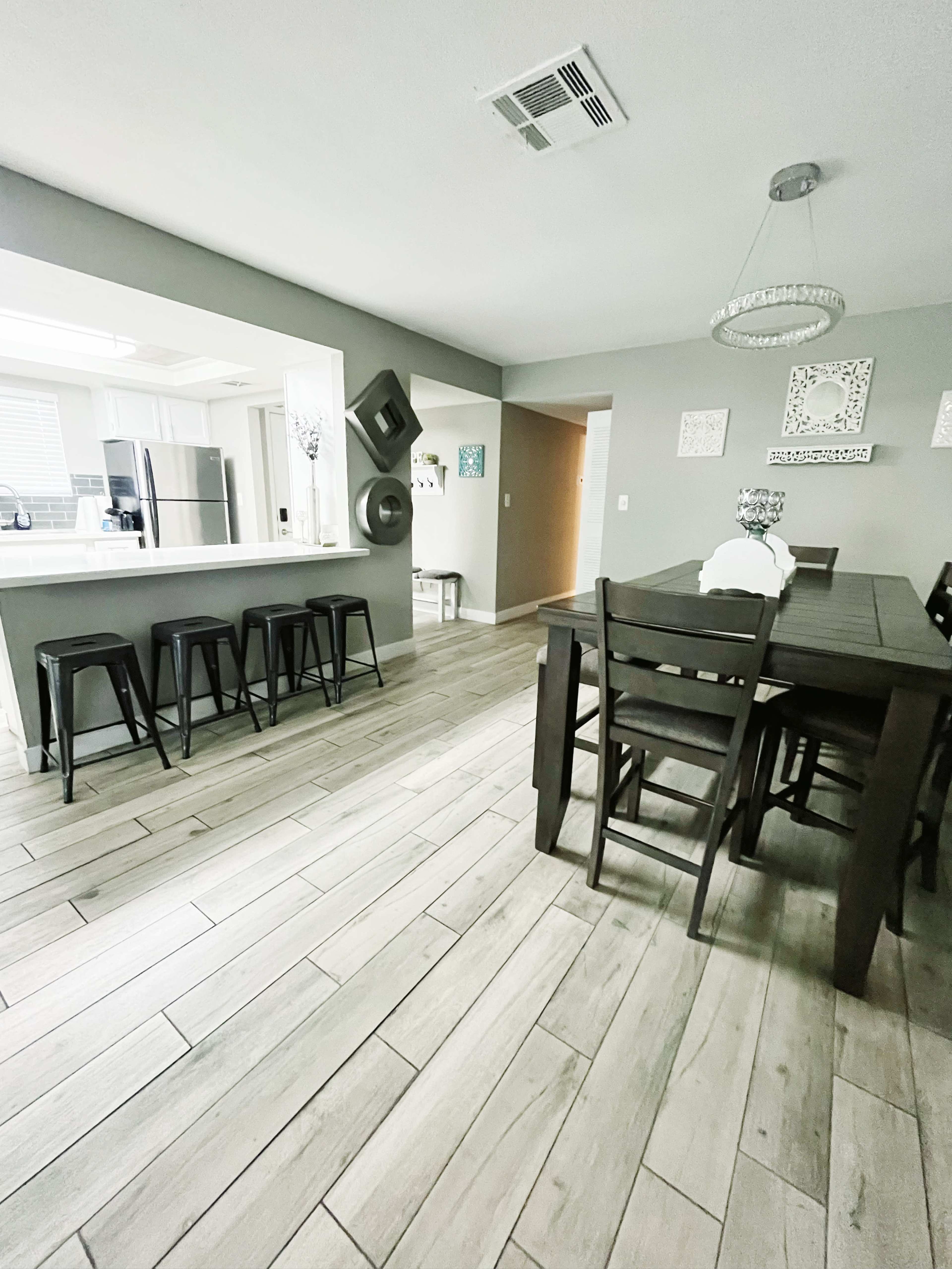 A modern dining area with a long table and black chairs, along with a kitchen visible in the background.