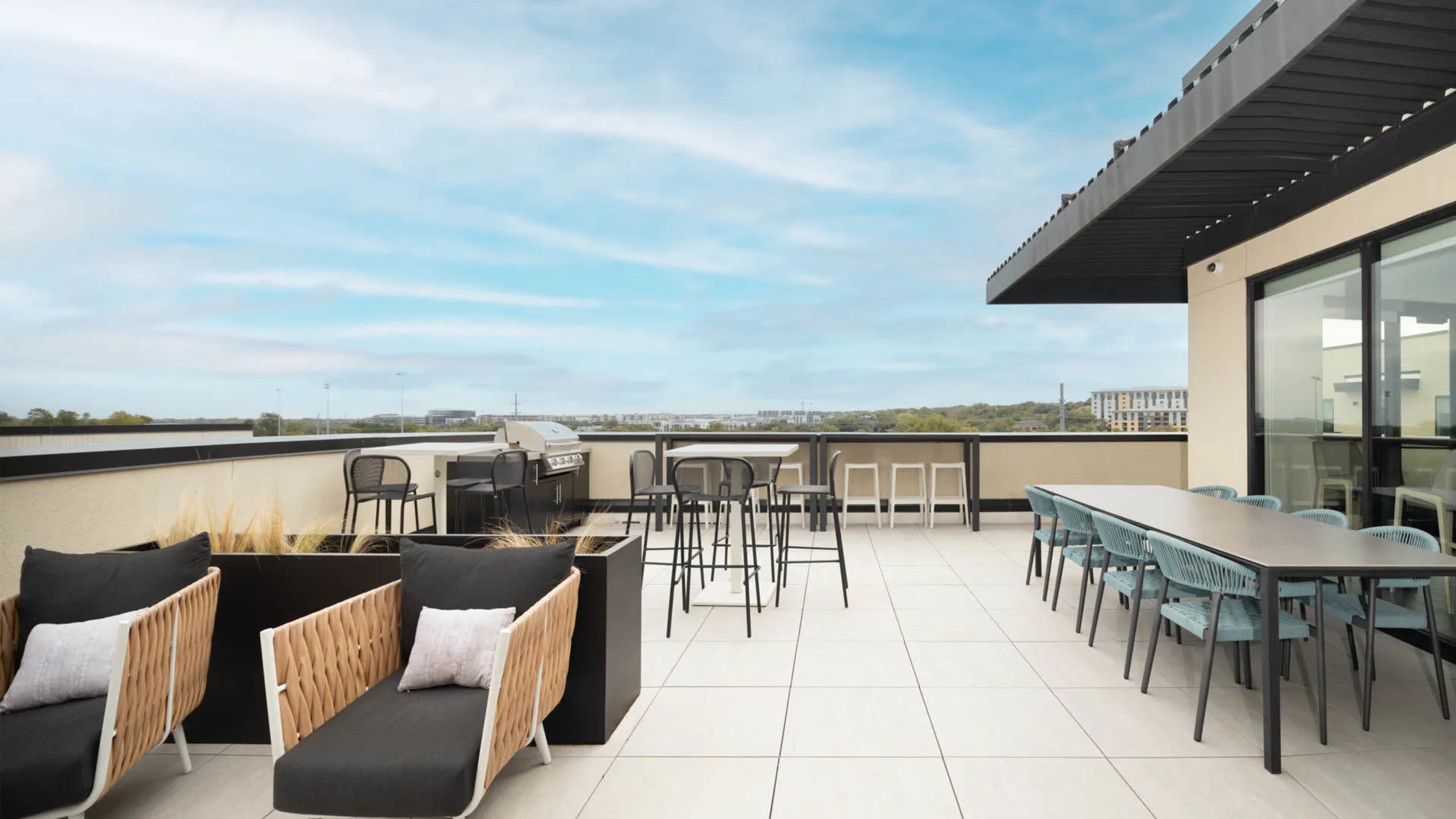 A spacious rooftop terrace featuring seating areas, a grill, and dining tables with a view of the surrounding landscape.
