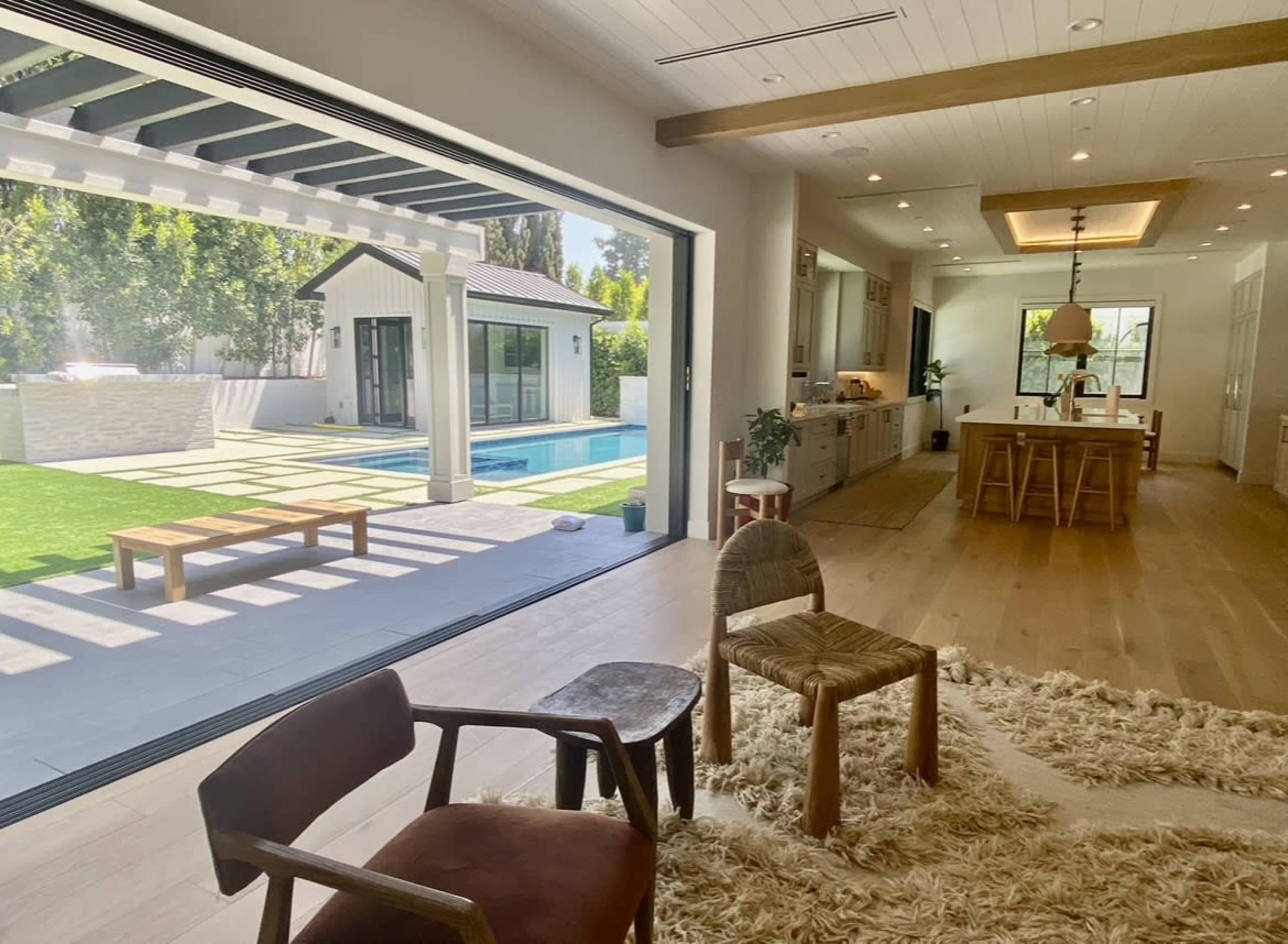 A spacious living area opens up to a backyard pool, featuring modern furnishings and a blend of indoor and outdoor spaces.