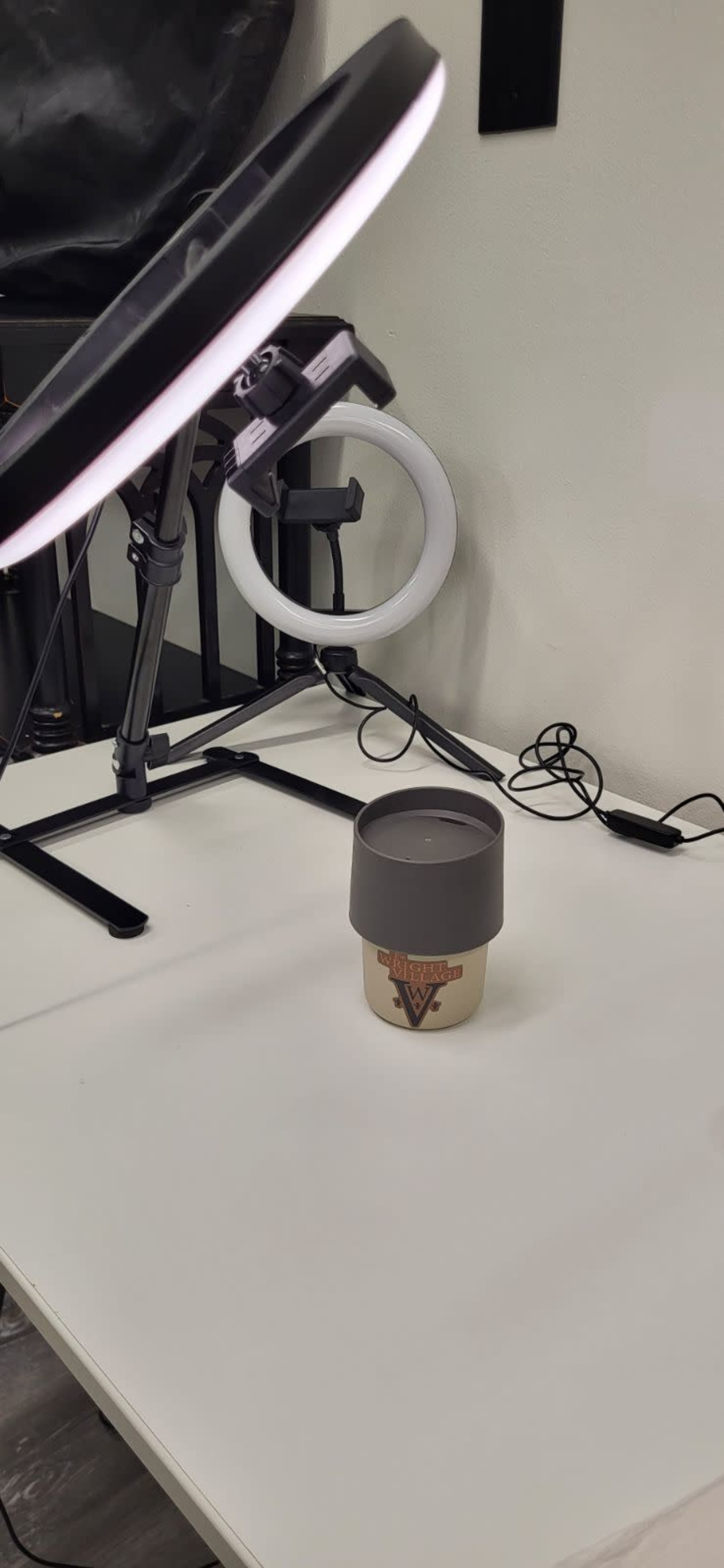 A coffee cup with a brown lid is placed on a table, beside a ring light.