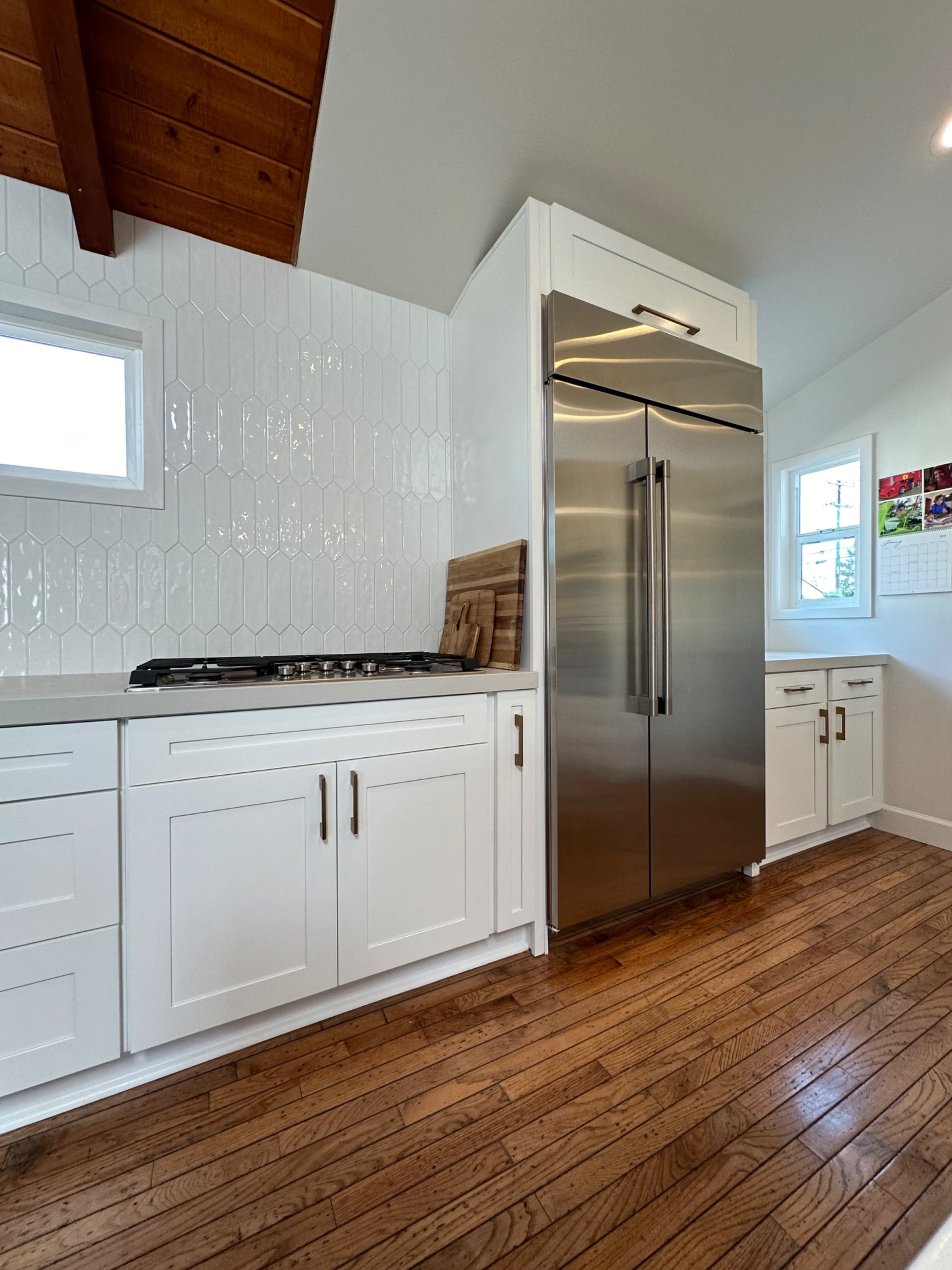 A modern kitchen features white cabinetry, a stainless steel refrigerator, and wood accents on the ceiling.