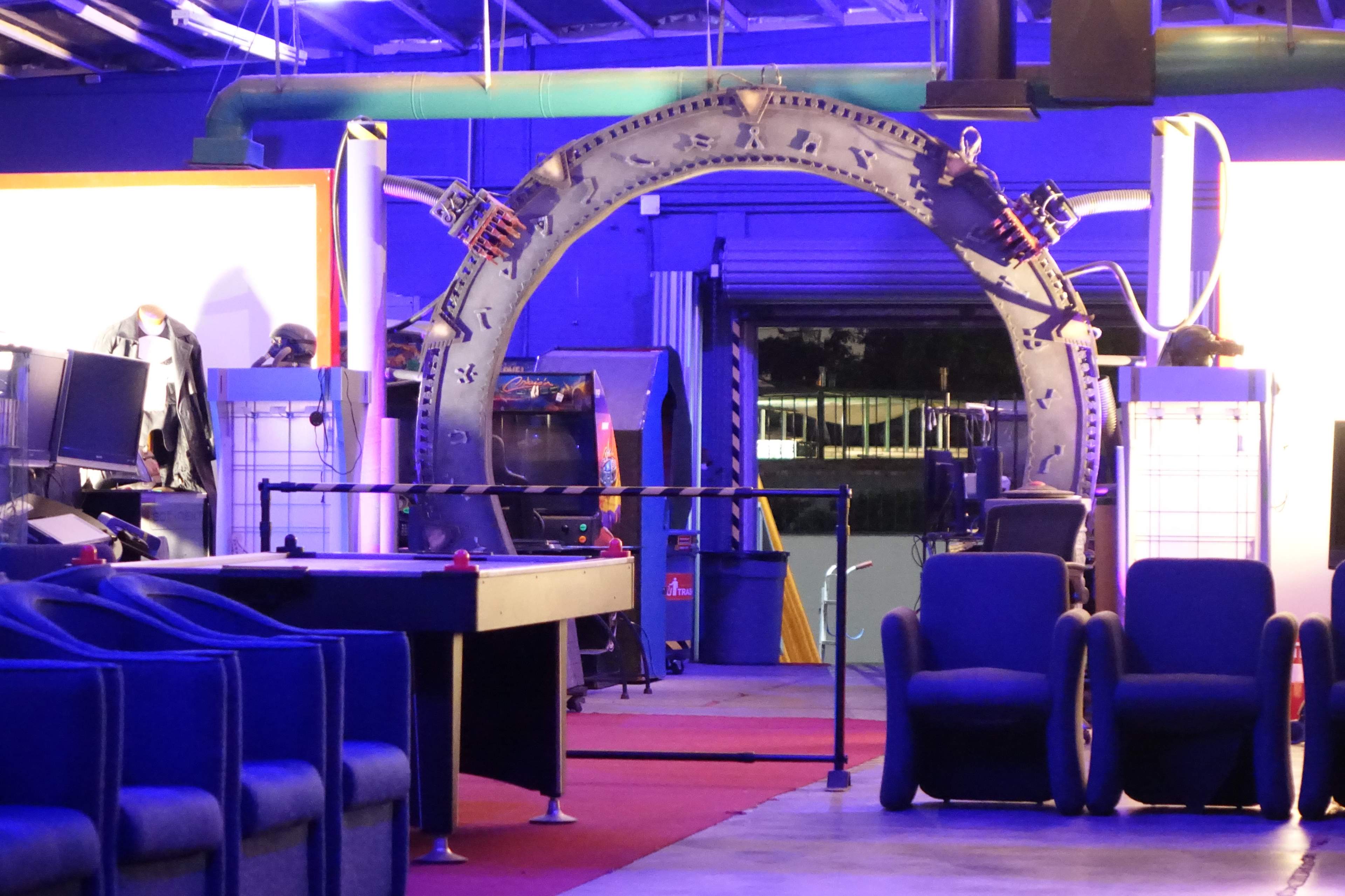 The image shows a brightly lit arcade area featuring an archway that resembles a stargate, with various gaming machines and blue seating in the foreground.