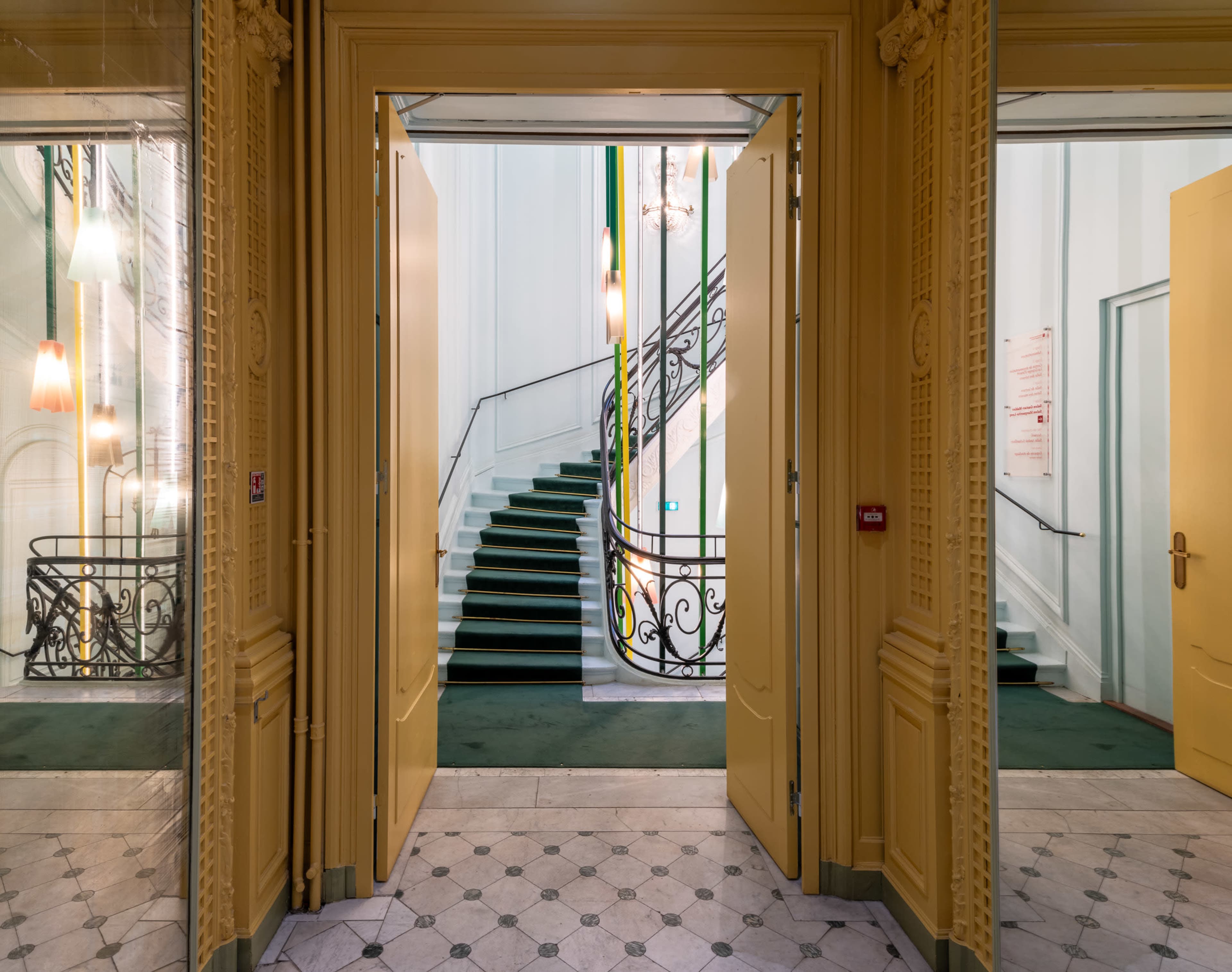 The image shows a spacious entrance with two open doors leading to a staircase, framed by decorative walls and a tiled floor.
