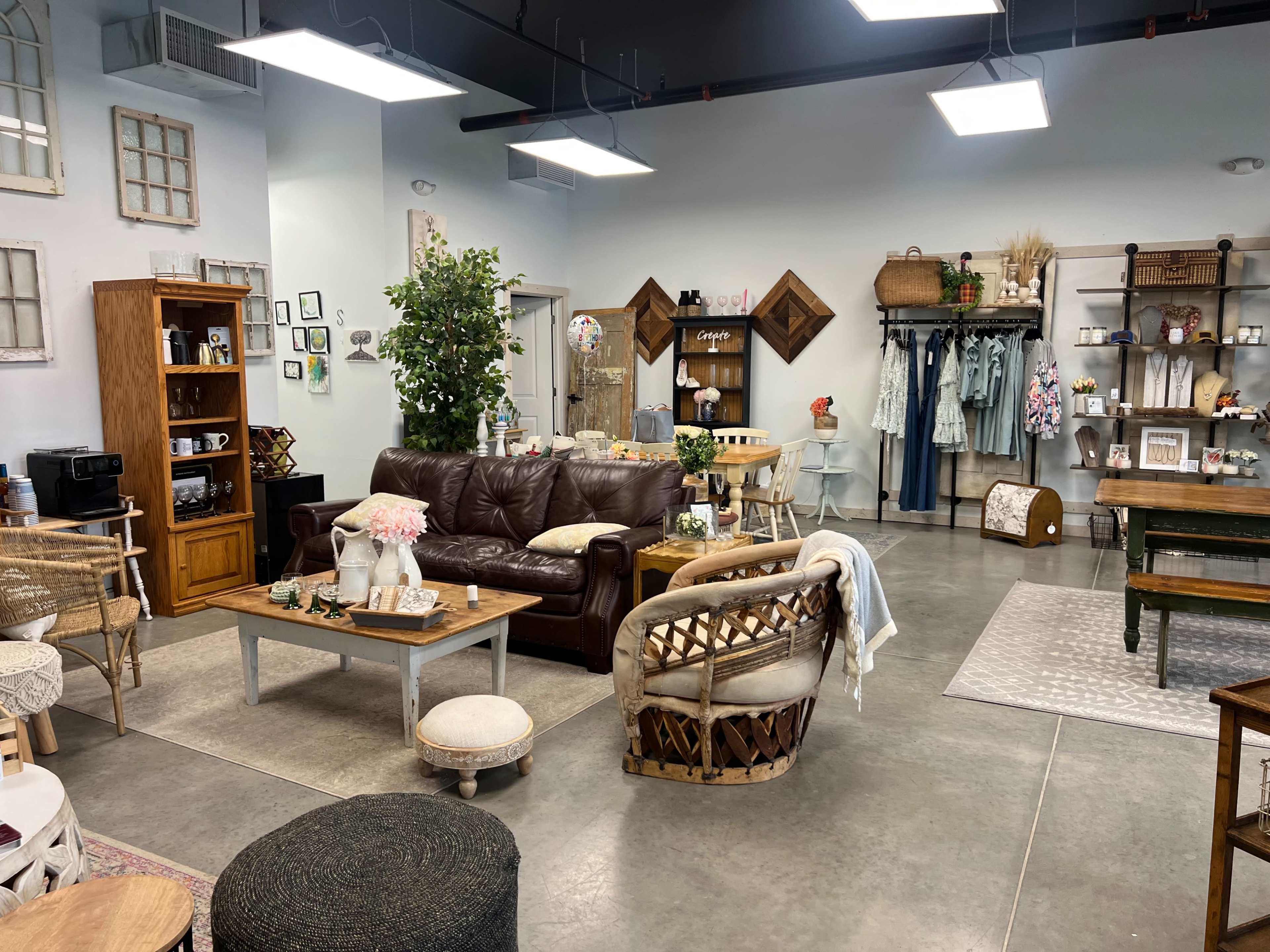 A cozy retail space featuring a brown leather couch, various wooden furniture pieces, decorative items, and a relaxed, inviting atmosphere.