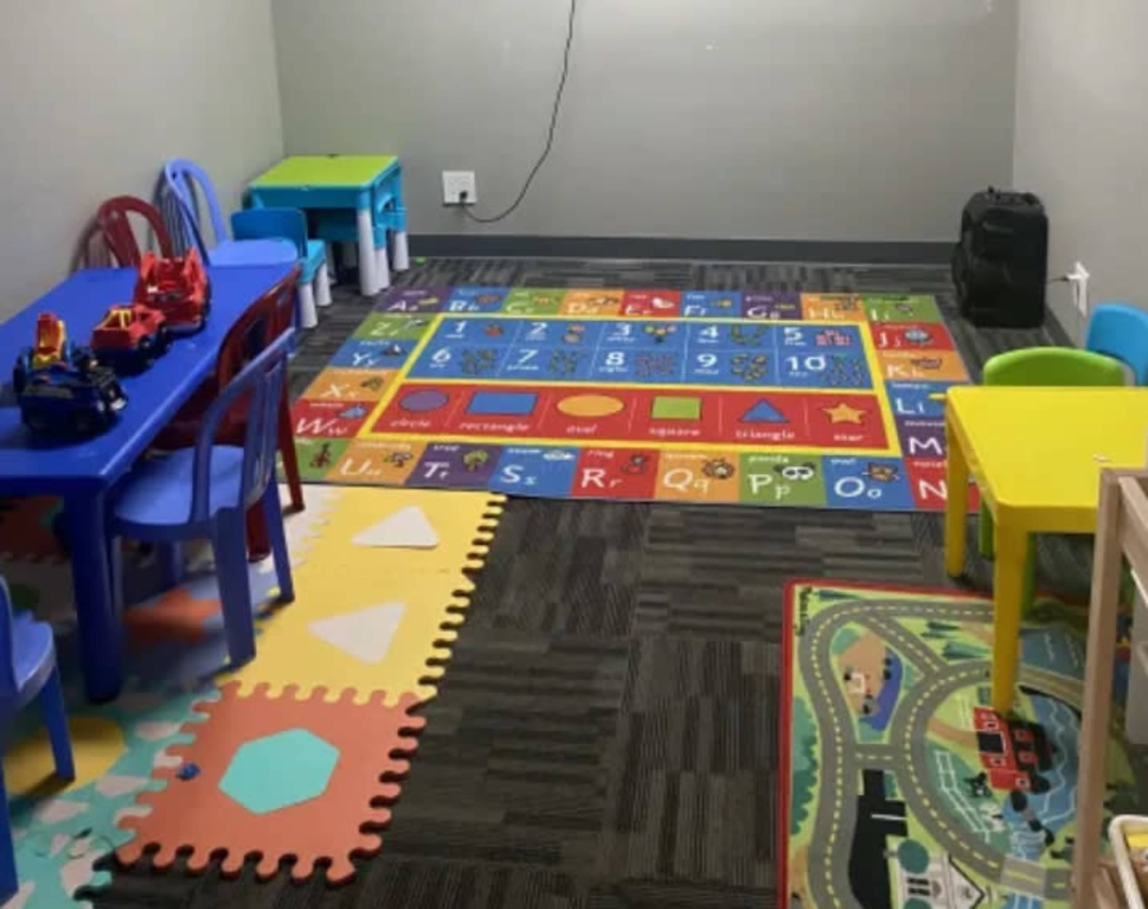A playroom with colorful rugs, toys on tables, and child-sized furniture arranged in the space.