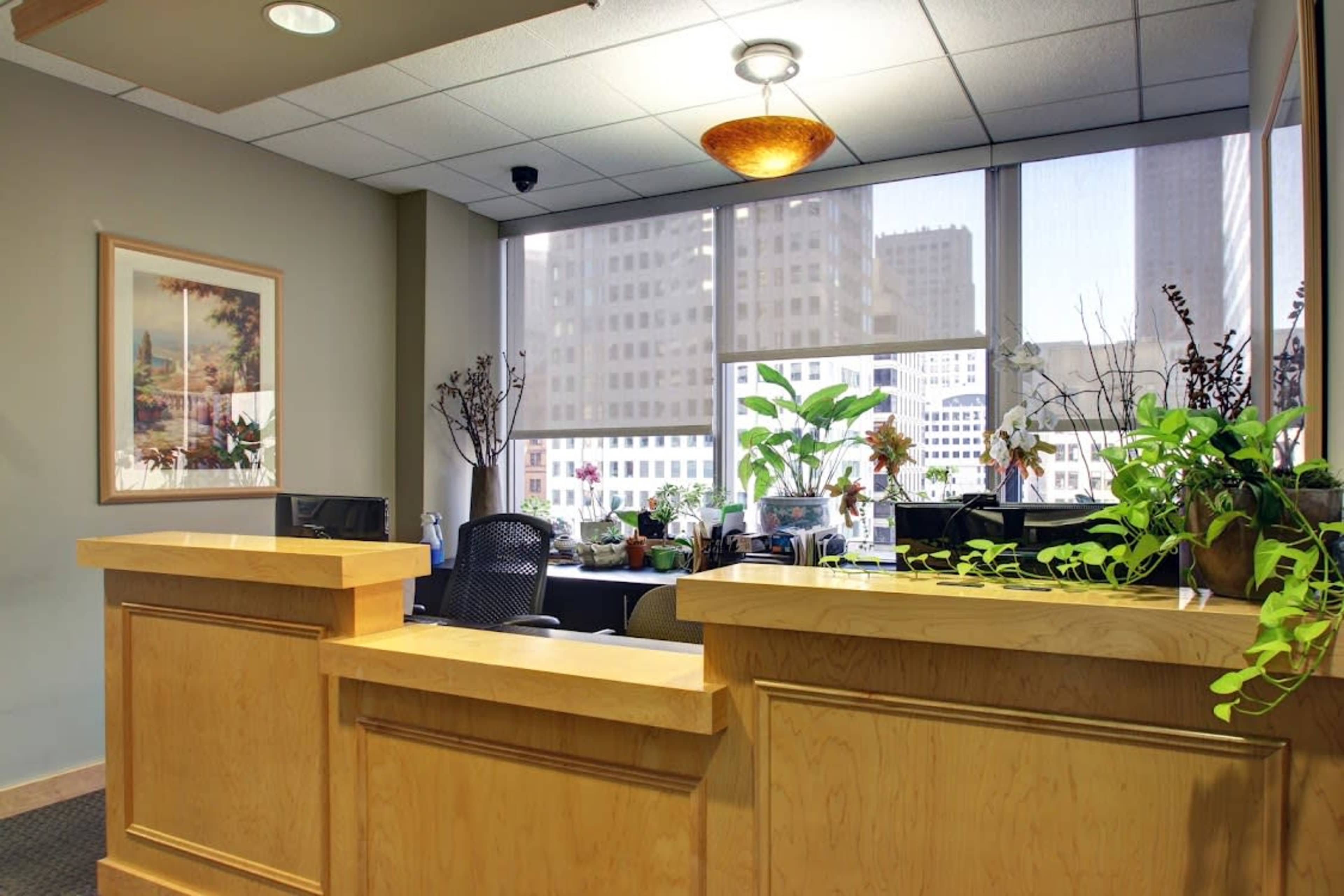 A reception area features a wooden countertop, plants, and computer workstations visible through large windows.