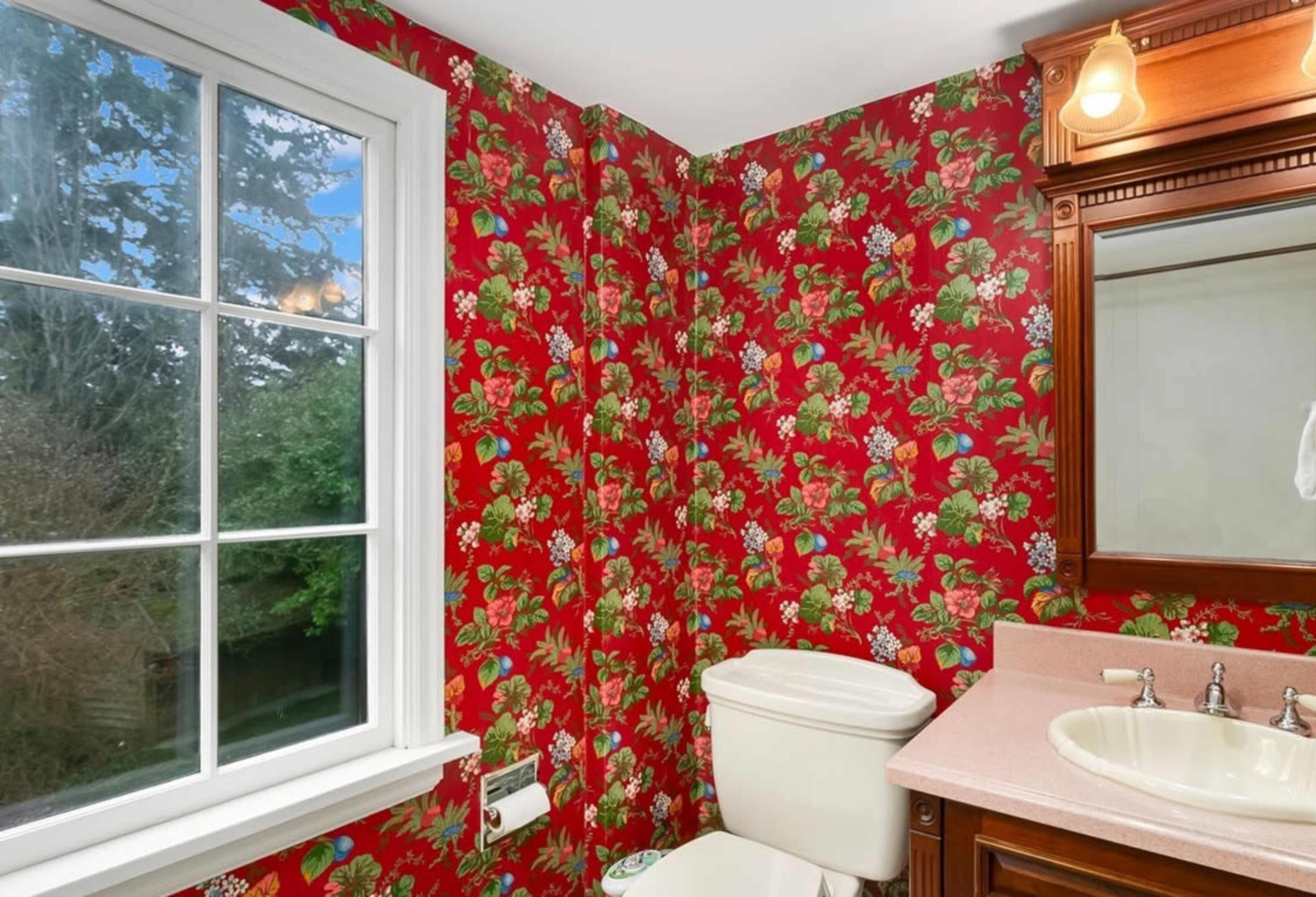 The bathroom features floral red wallpaper, a white toilet, and a sink with a wooden mirror above it.