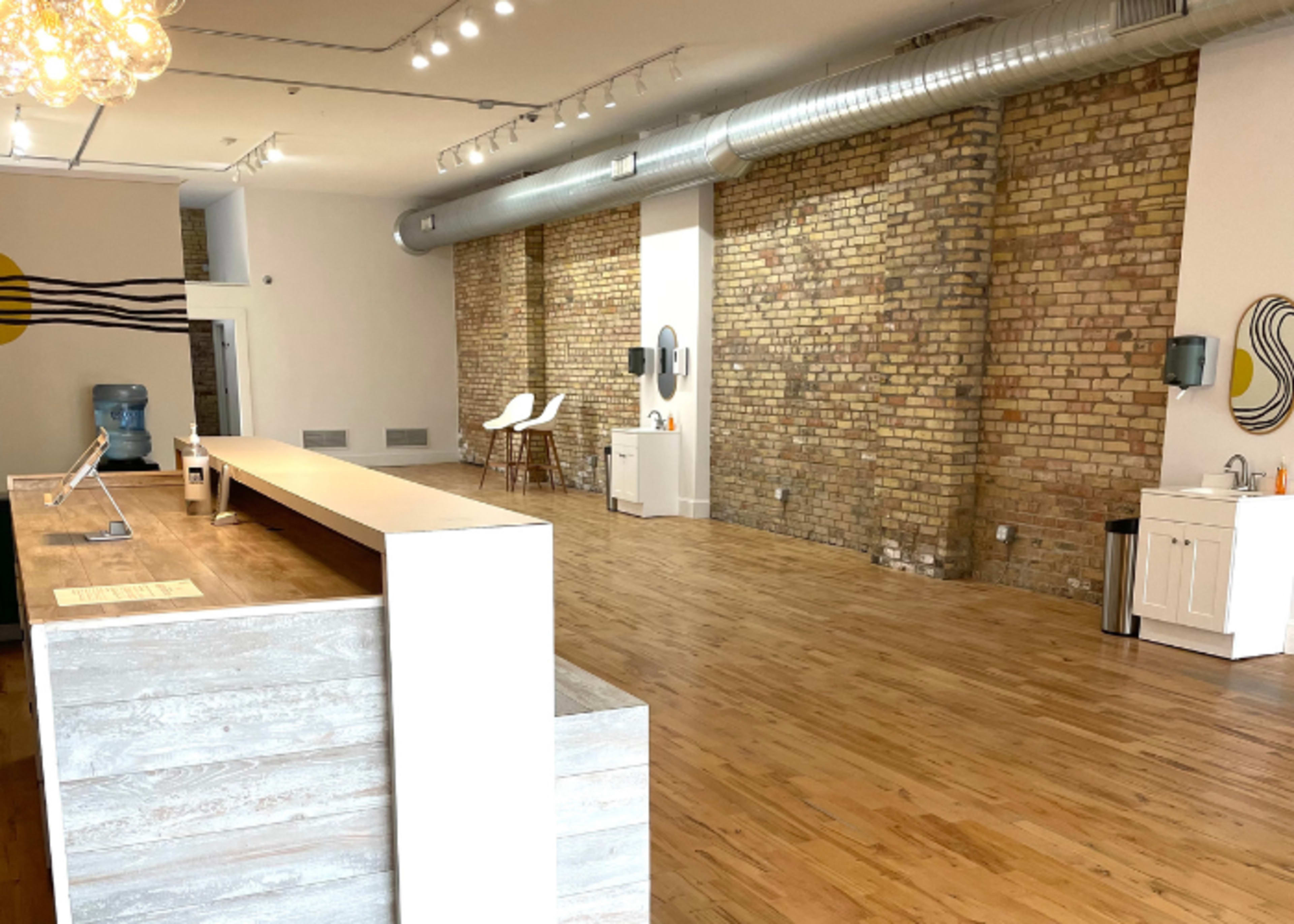 A spacious interior with exposed brick walls, wooden flooring, and a minimalist reception area featuring a long counter and a water cooler.