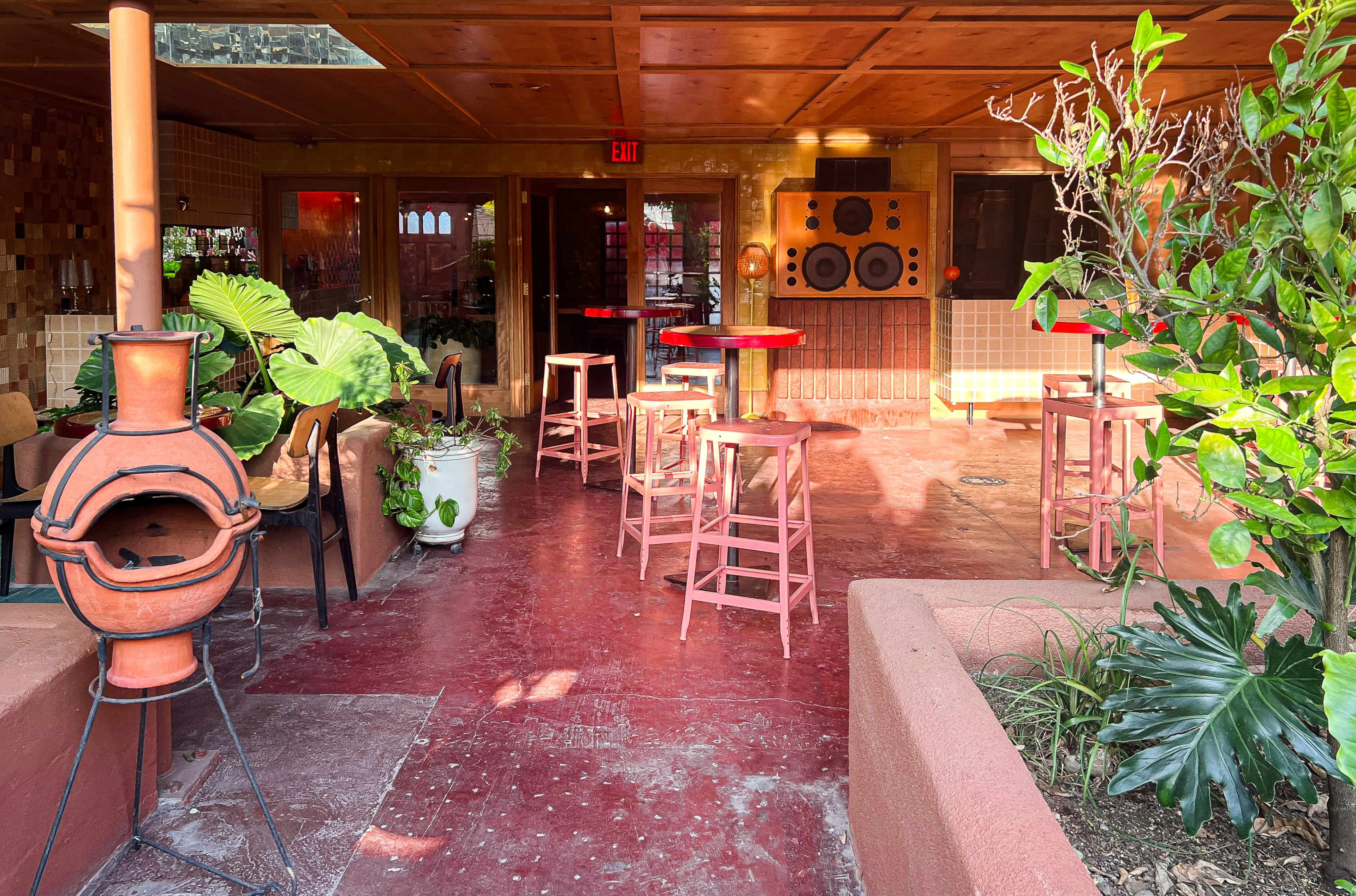 An indoor space with several wooden stools, a traditional clay chiminea, and potted plants surrounding a red-themed area.