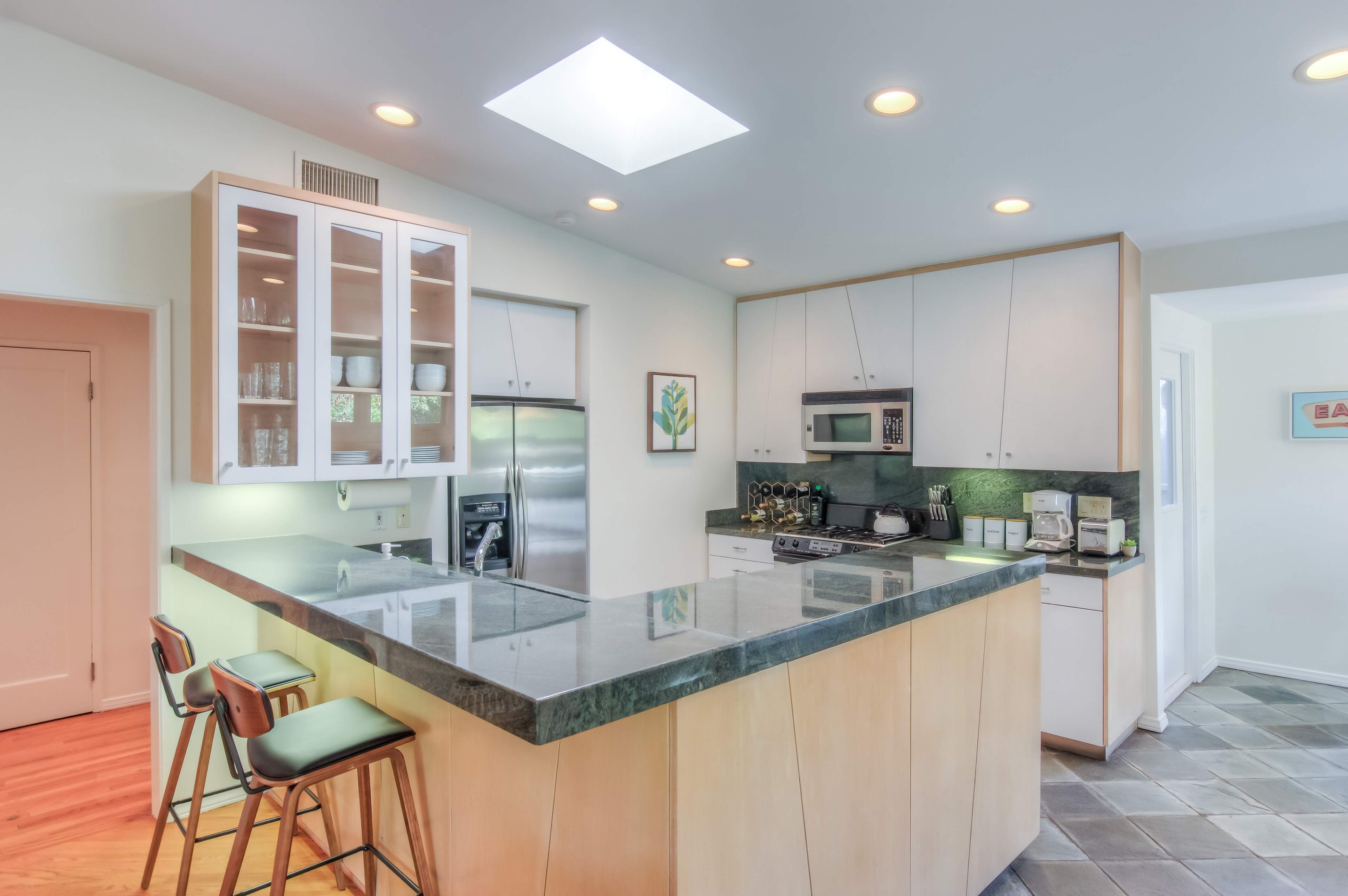 A modern kitchen features a central island with bar stools, stainless steel appliances, and a skylight for natural light.