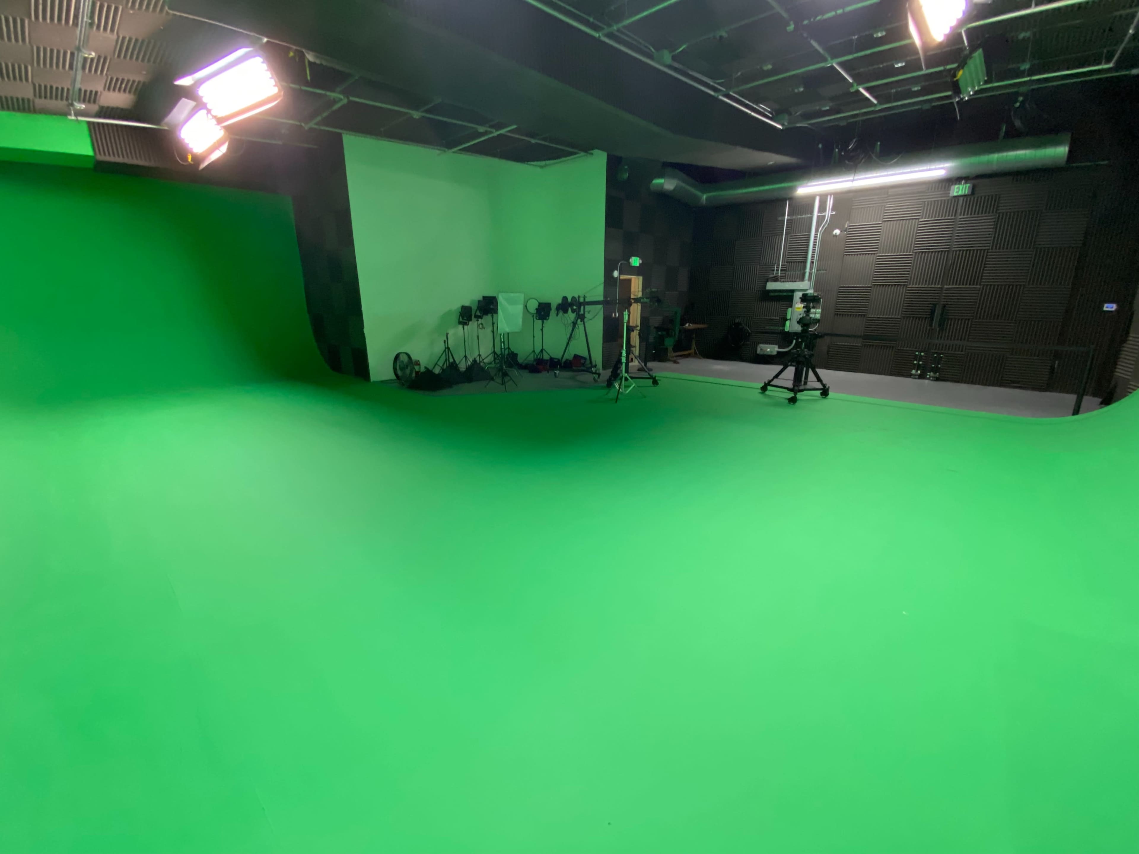 A green screen studio with a large green backdrop and studio equipment arranged against the walls.