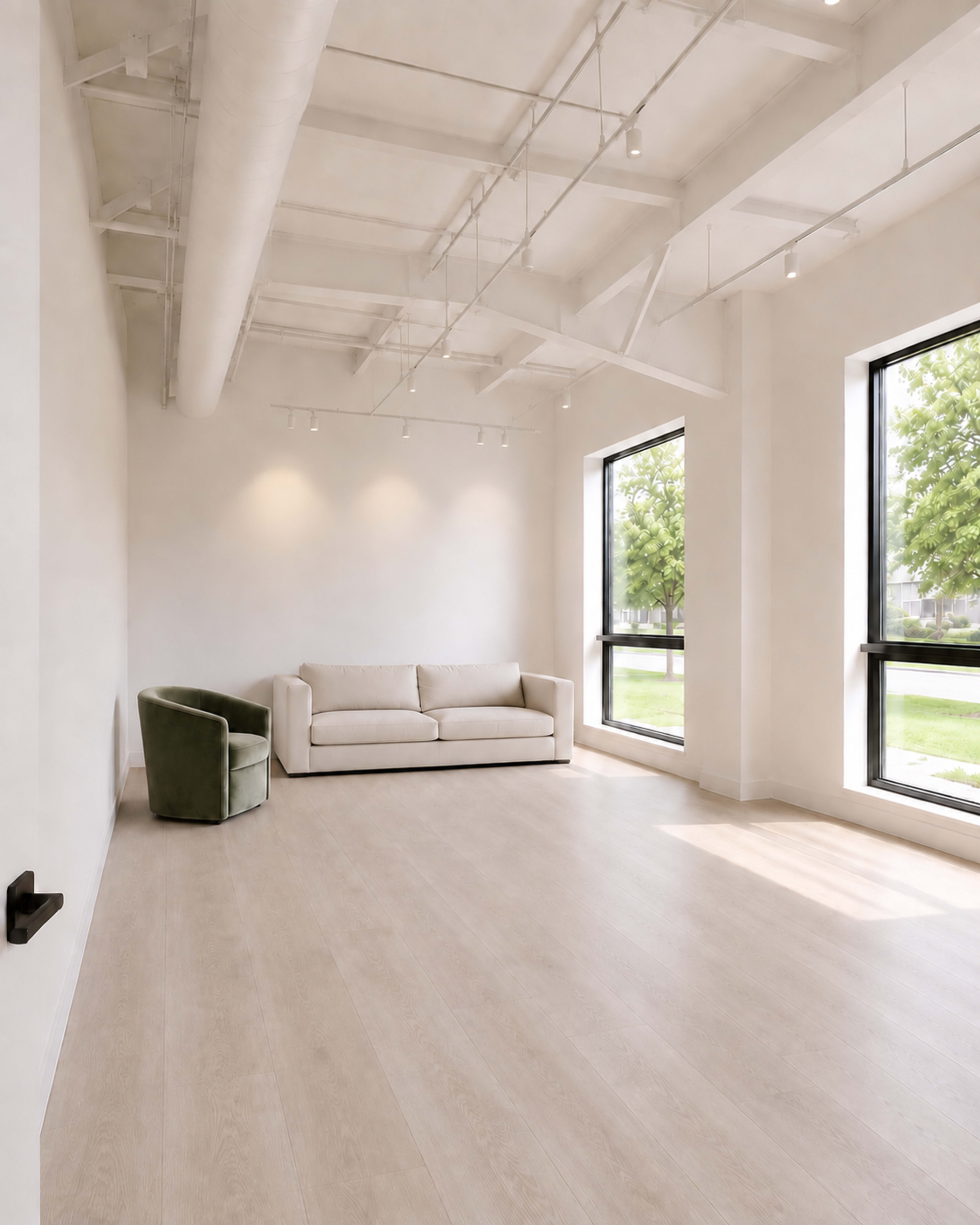 The image shows a minimalistic interior space featuring a green armchair and a light-colored sofa, with large windows allowing natural light to illuminate the room.