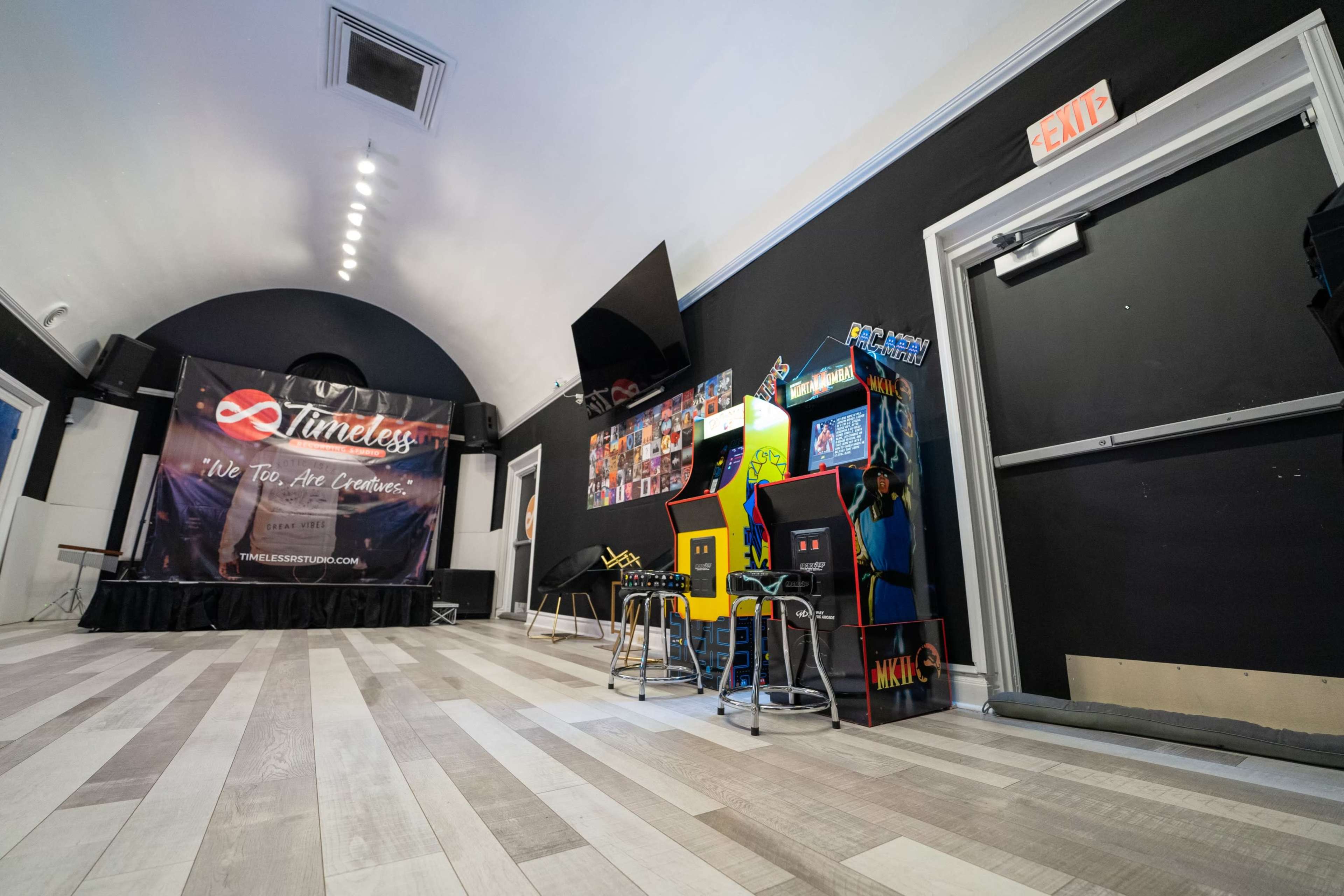 The image shows a spacious entertainment room featuring arcade machines, a stage area with a backdrop, and seating arrangements.