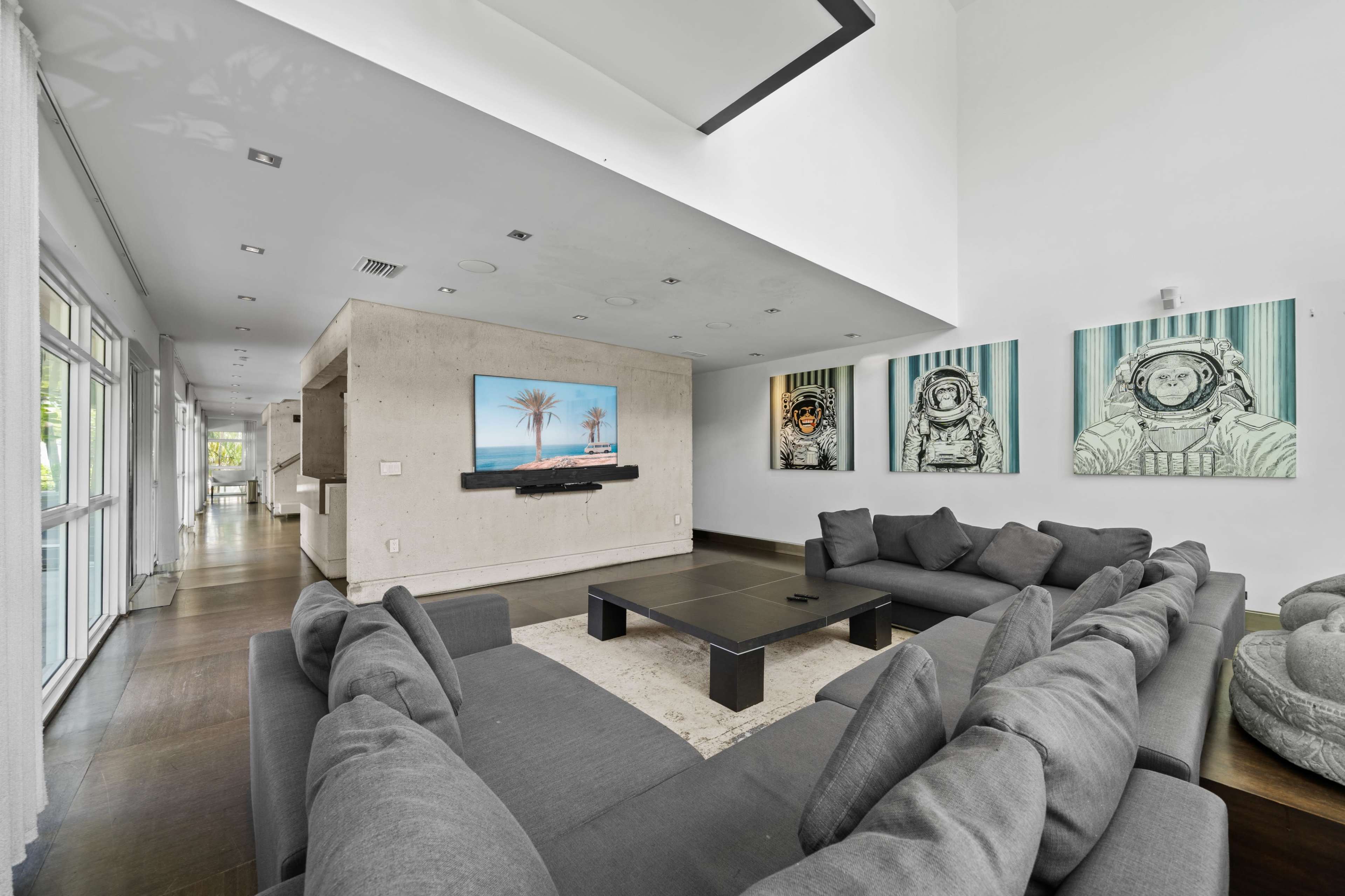 The room features a modern living area with a large sectional sofa, a flat-screen TV mounted on the wall, and abstract art of astronauts on the adjacent wall.