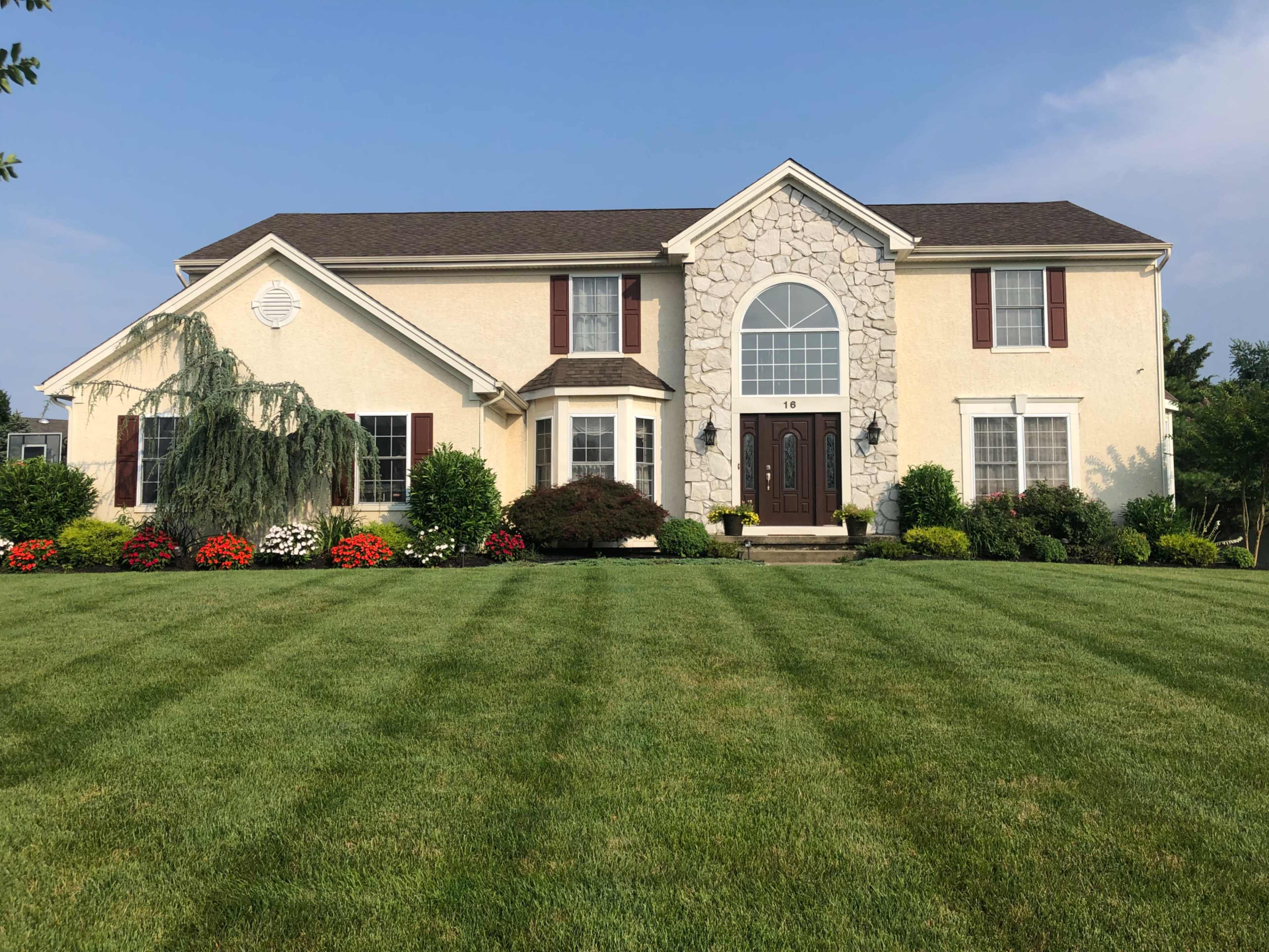 A two-story house featuring a stone facade, manicured lawn, and colorful flower beds.
