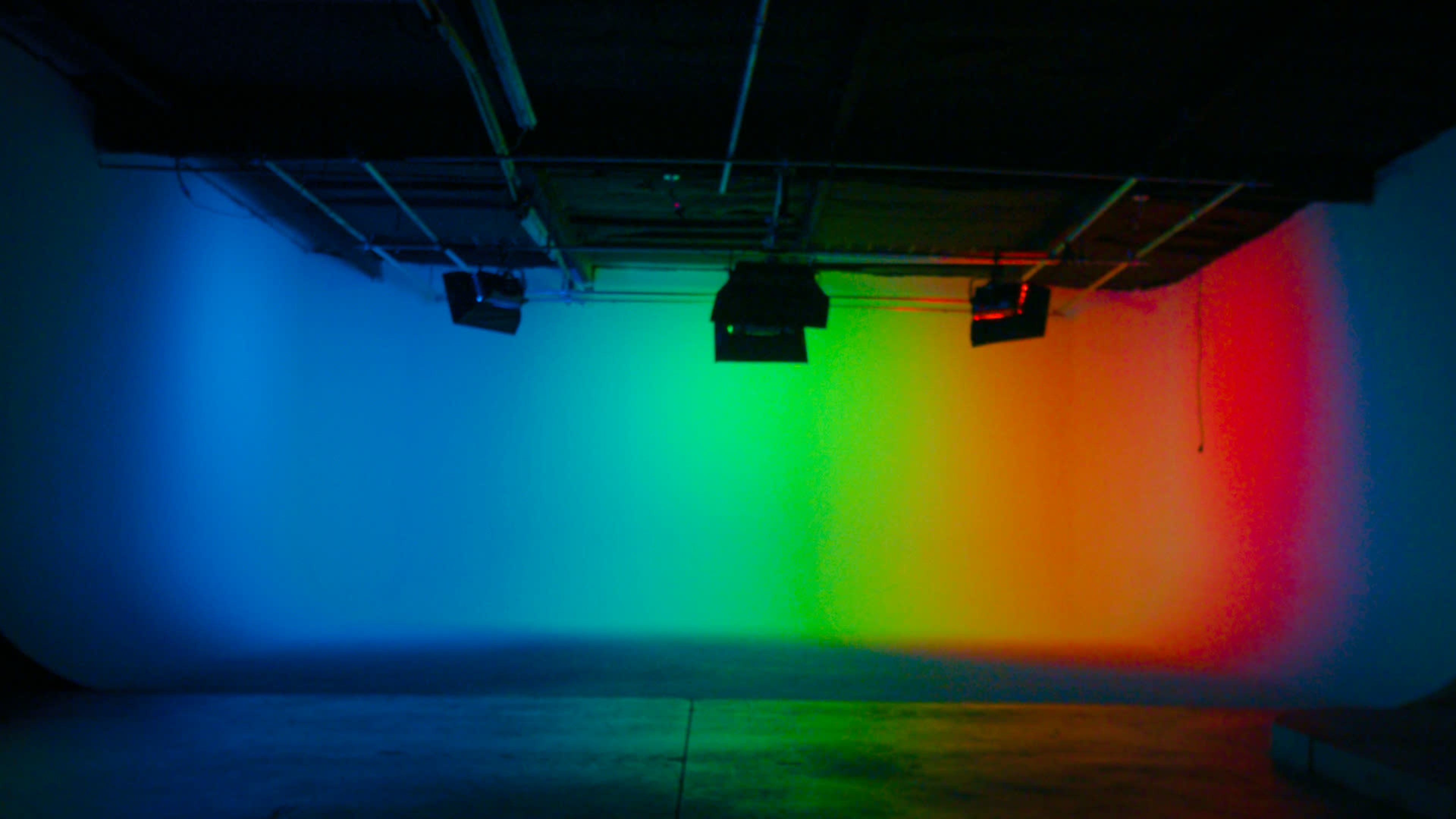 A studio space is illuminated with a gradient of colored lights transitioning from blue to green to orange on the walls.