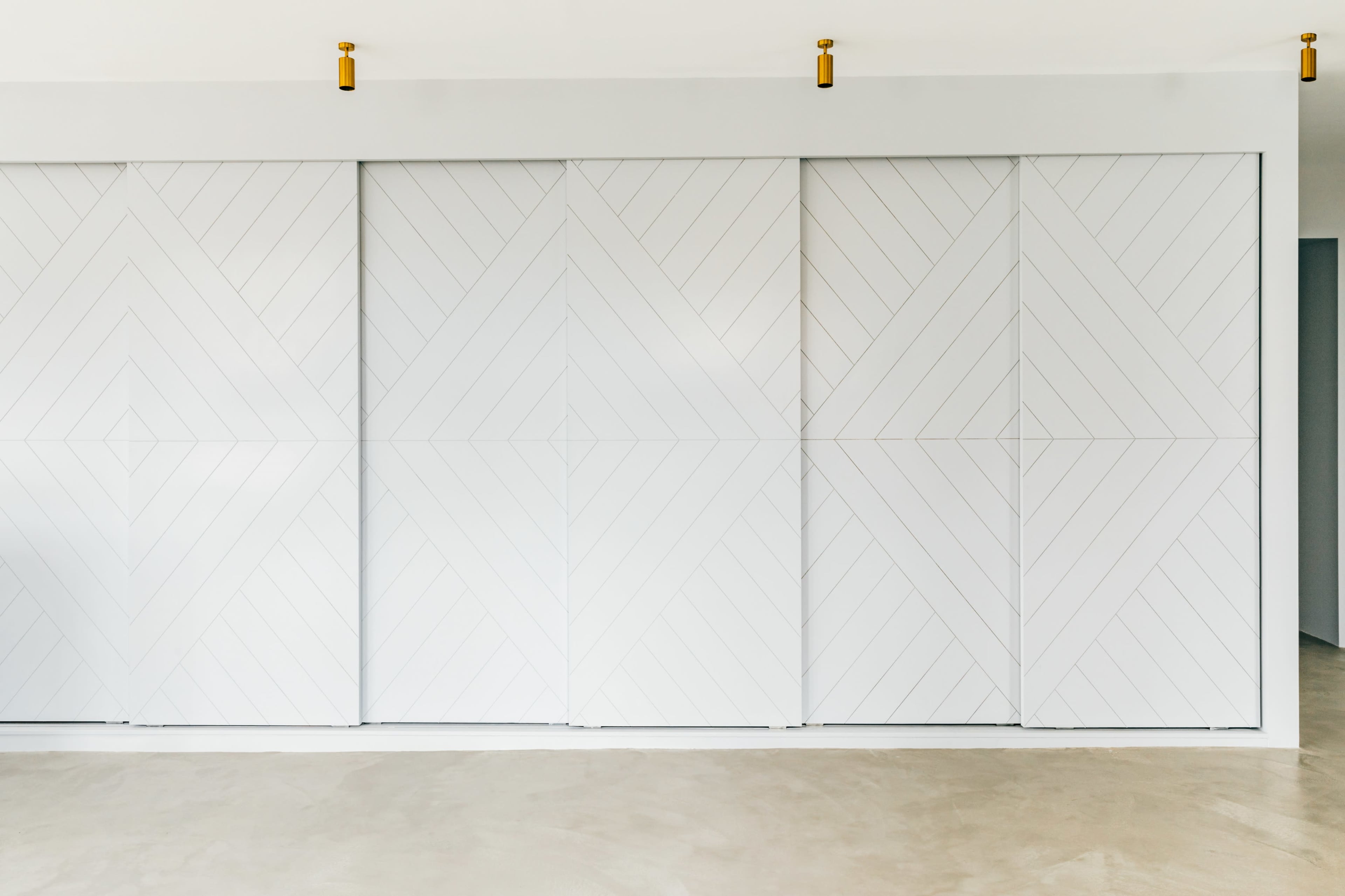 A minimalist interior with three large white sliding doors featuring a geometric design.