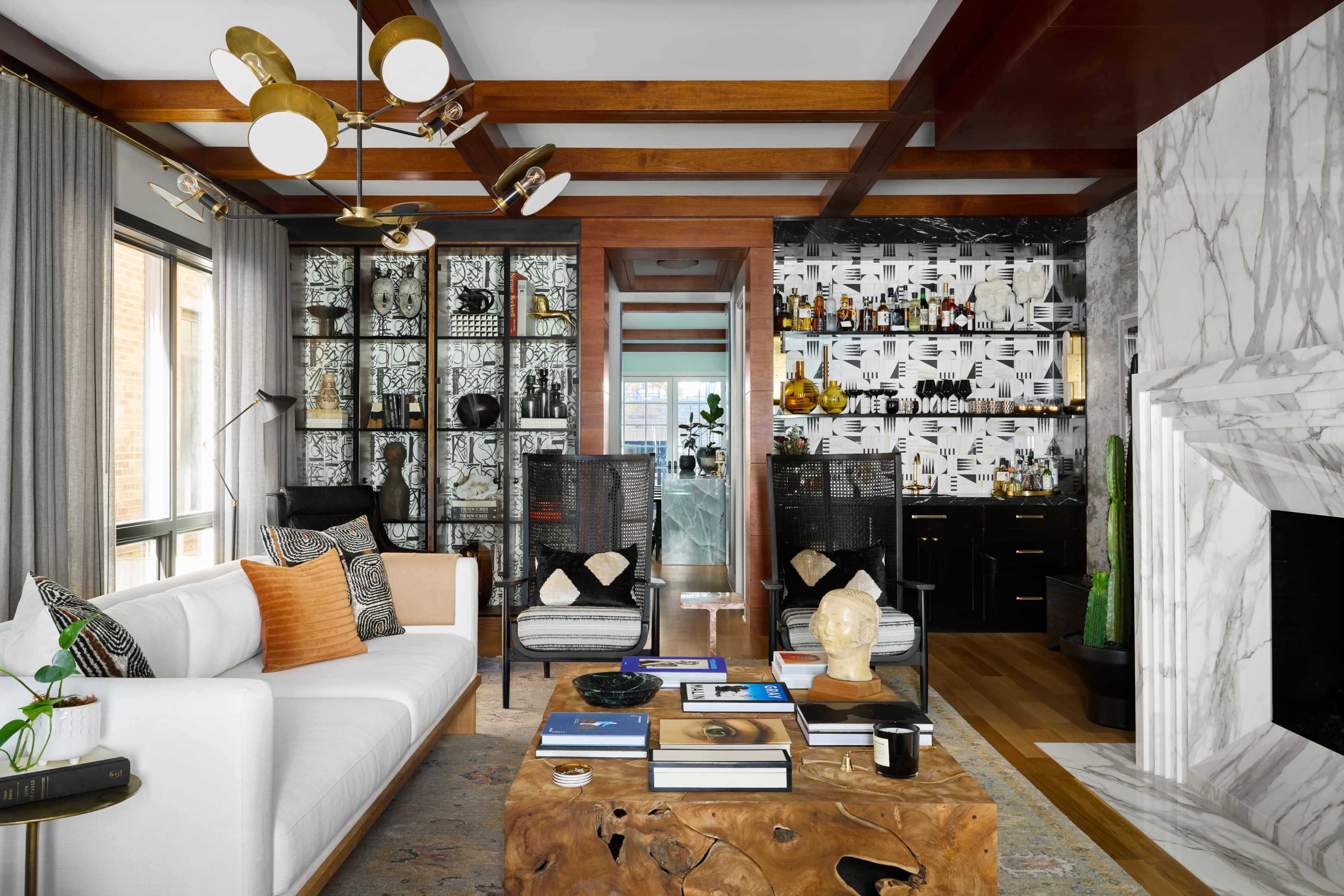 A modern living room features a white sofa, a large wooden coffee table, and stylish decor against a backdrop of patterned wallpaper and a marble fireplace.